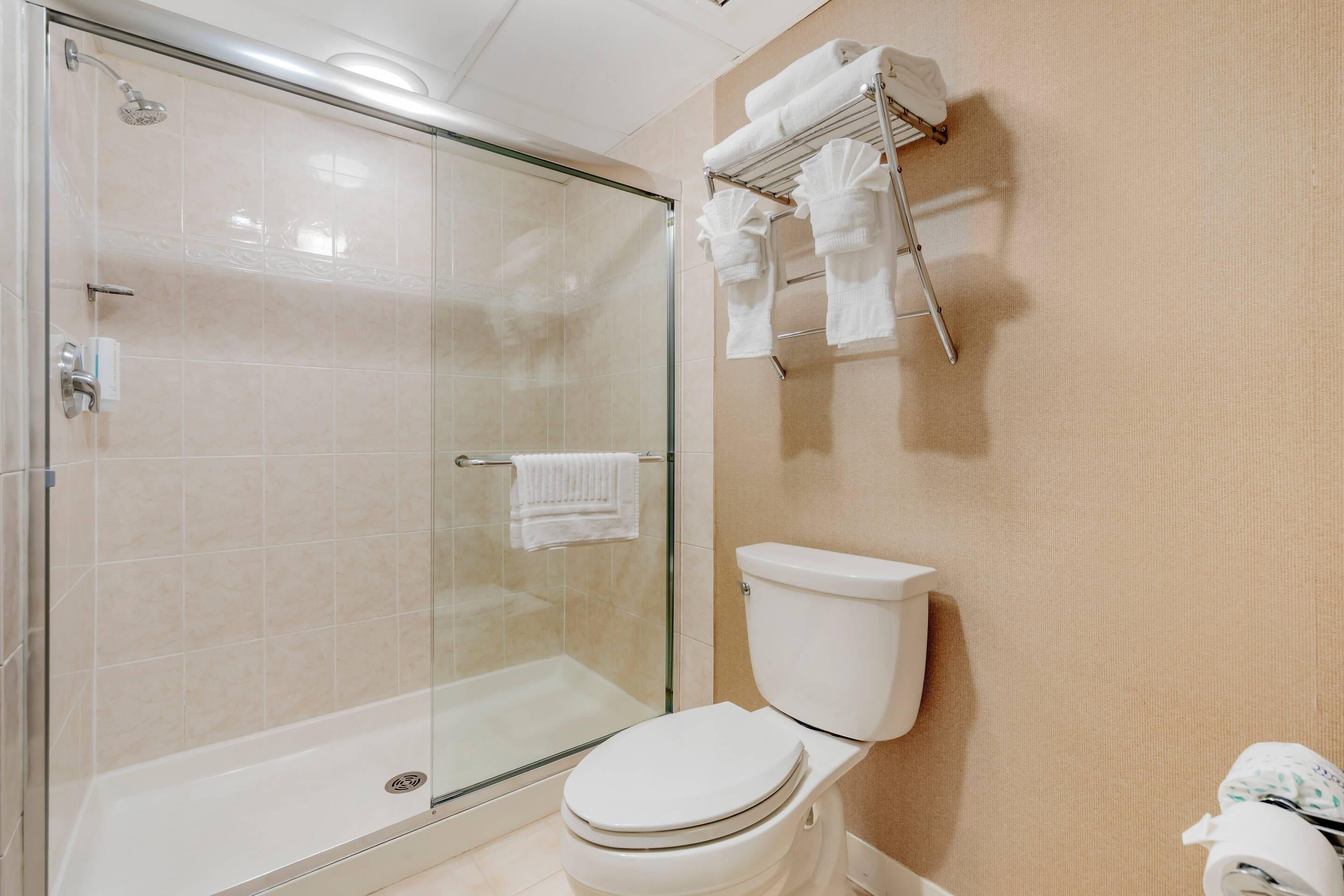 Un baño moderno con ducha de vidrio, inodoro blanco y toallero con varias toallas.