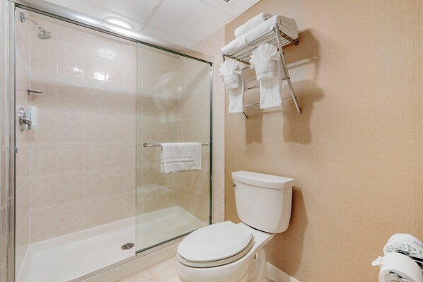 Un baño moderno con ducha de vidrio, inodoro blanco y toallero con varias toallas.