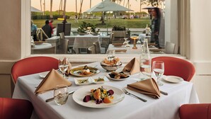 A dining table with plates of food, cutlery, and glasses, set against a window with a view of palm trees and a sign reading 'KOLAVA'. - Avalon Hotel (Miami Beach)