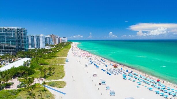A beach with a row of beach umbrellas and lounge chairs, a white sandy beach, and a clear blue ocean. - Avalon Hotel (Miami Beach)
