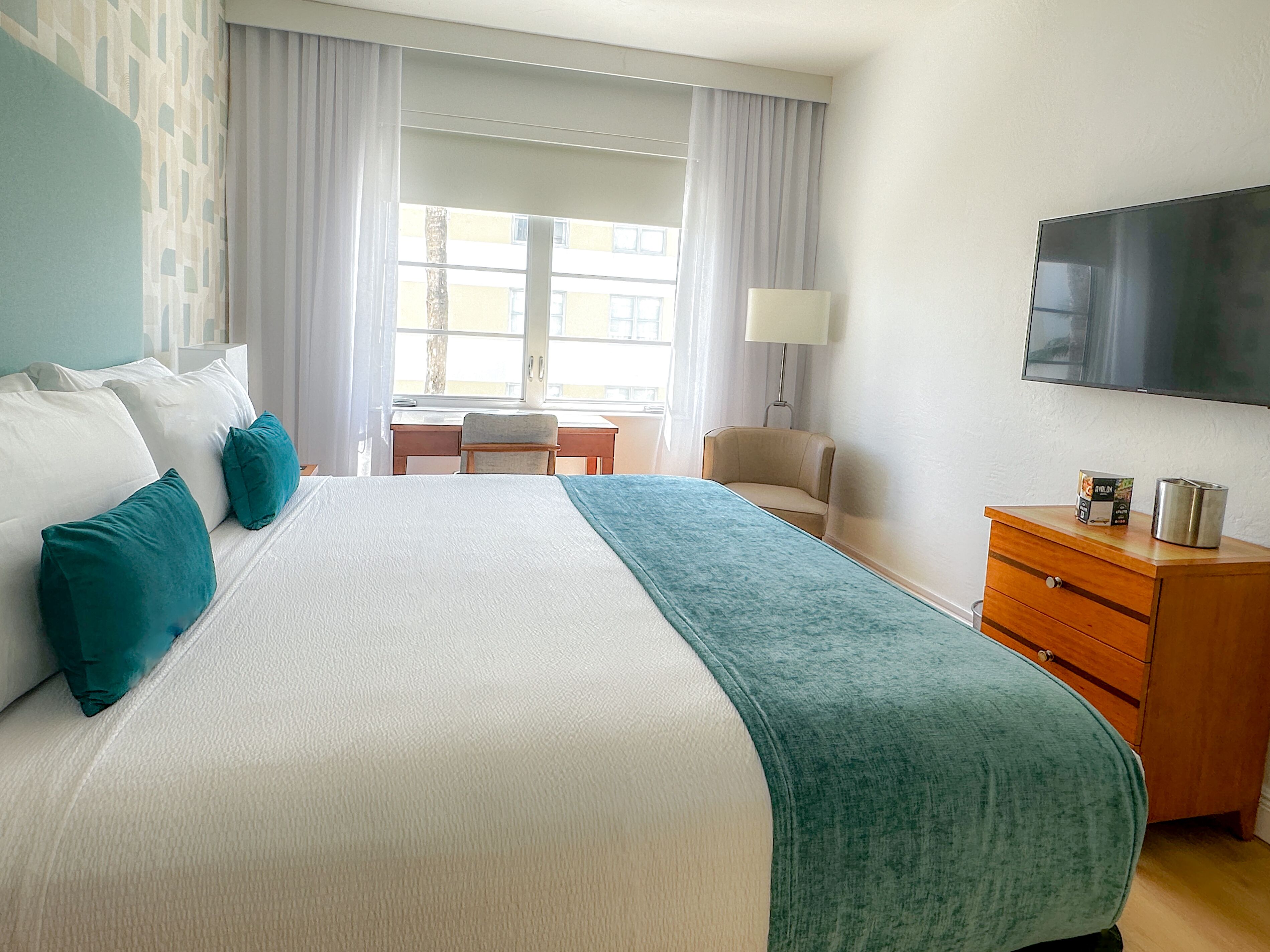 Ein Hotelzimmer mit einem großen Bett, einem Schreibtisch, einem Stuhl, einem Fernseher und einer Holzkommode.