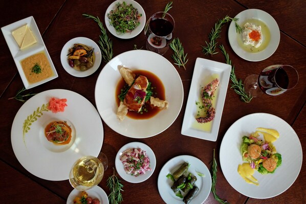 A variety of dishes on a wooden table, including a plate with a fish dish, a bowl of soup, and several small plates with different foods.
