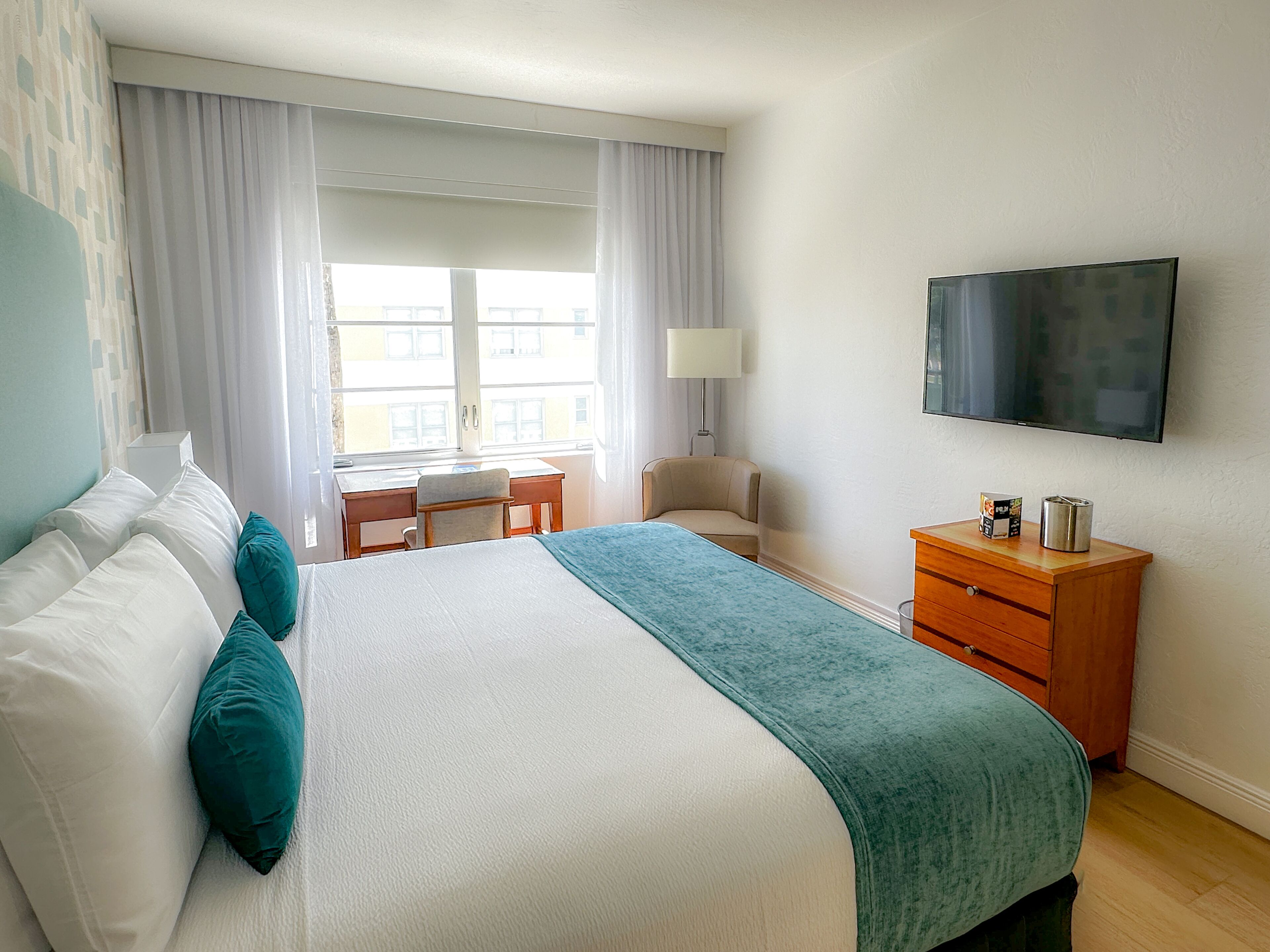Ein Hotelzimmer mit Bett, Schreibtisch, Stuhl, Fernseher und Kommode.