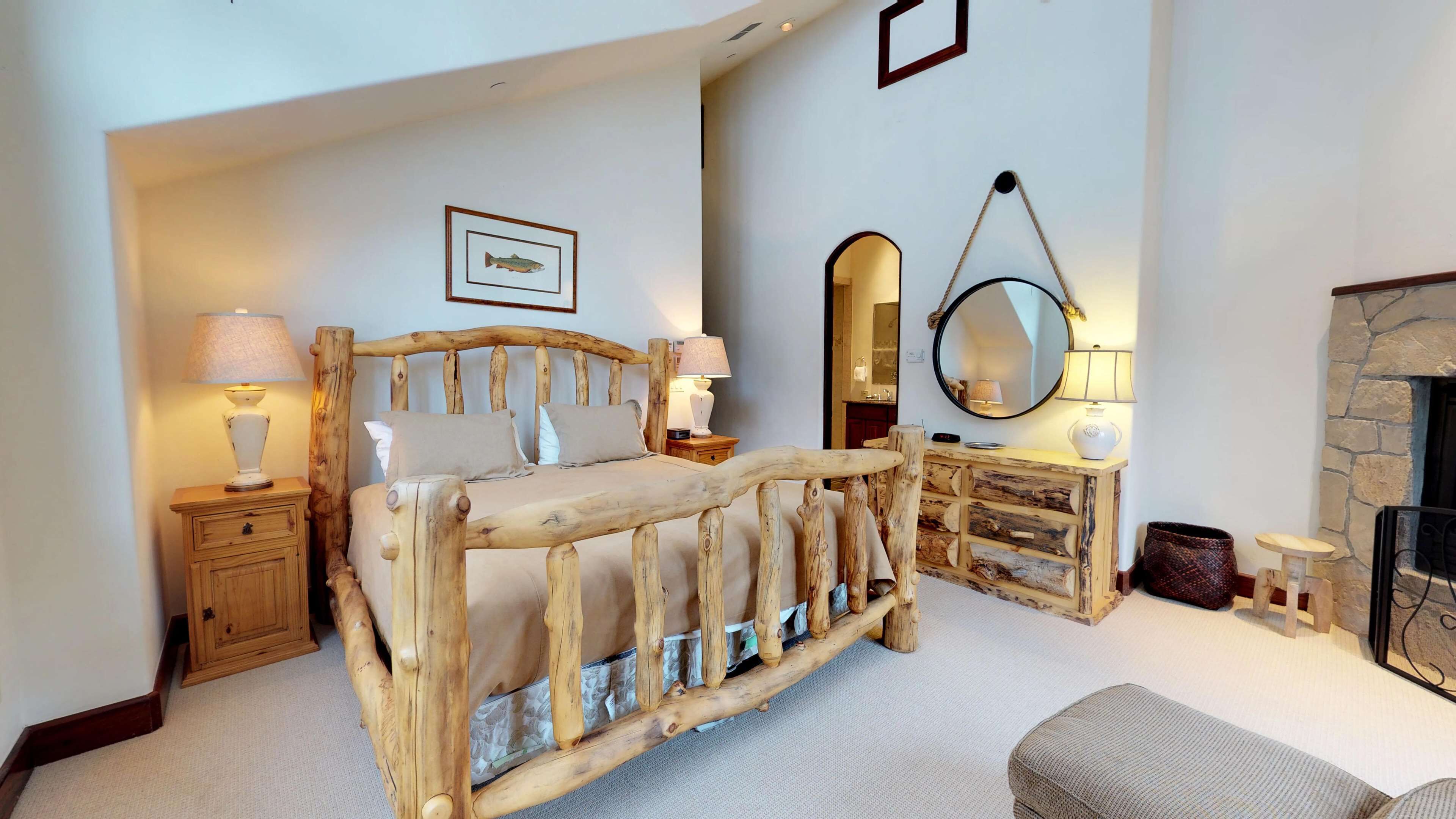 A bedroom with a rustic wooden bed, a stone fireplace, and a mirror on the wall.