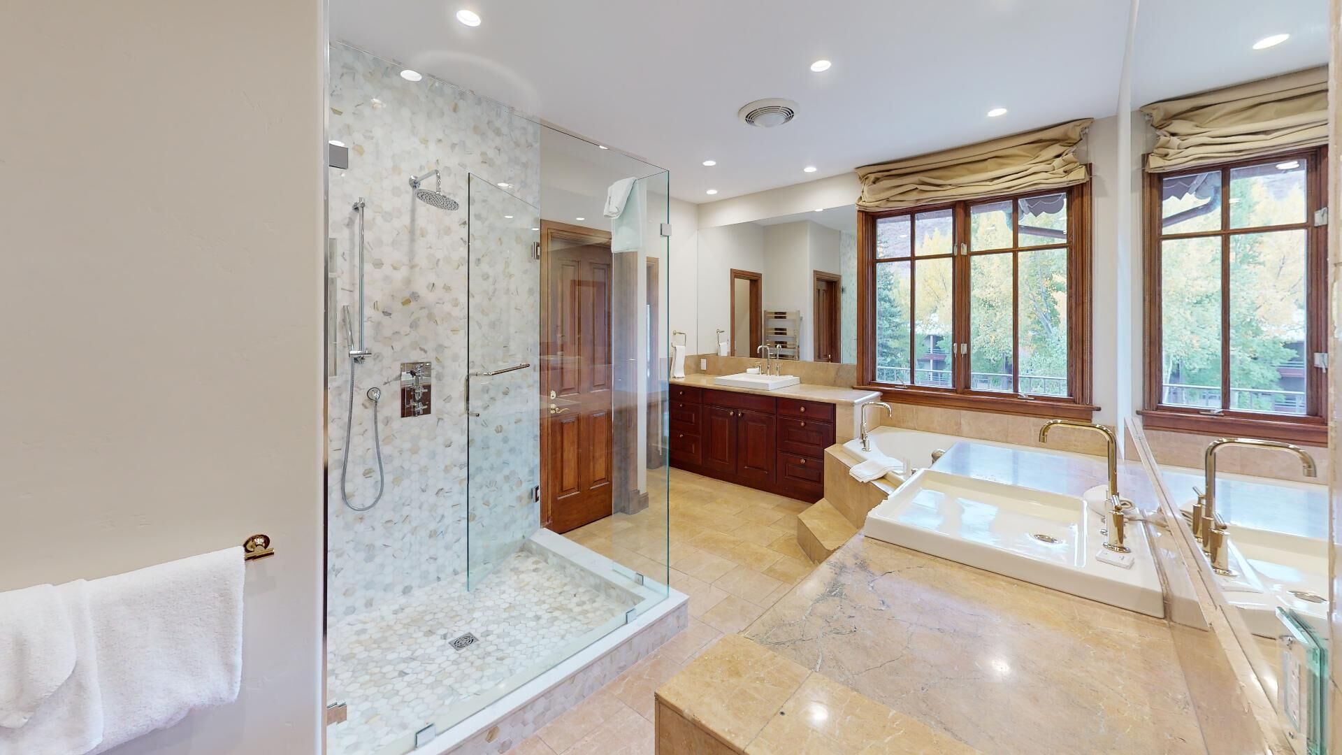 Un bany modern amb plat de dutxa envoltat de vidre, una banyera gran i un lavabo amb rentaperxes.
