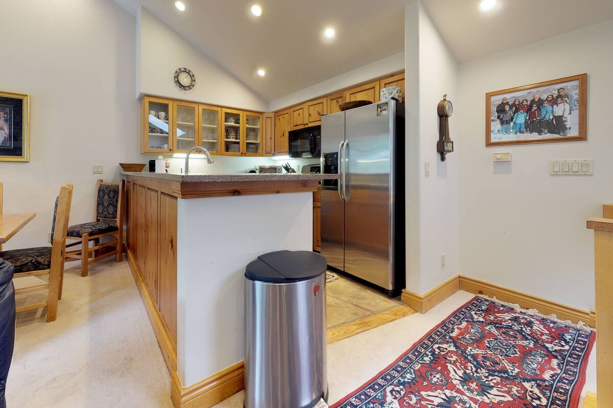 A modern kitchen with wooden cabinets, a stainless steel refrigerator, and a dining area with a table and chairs.