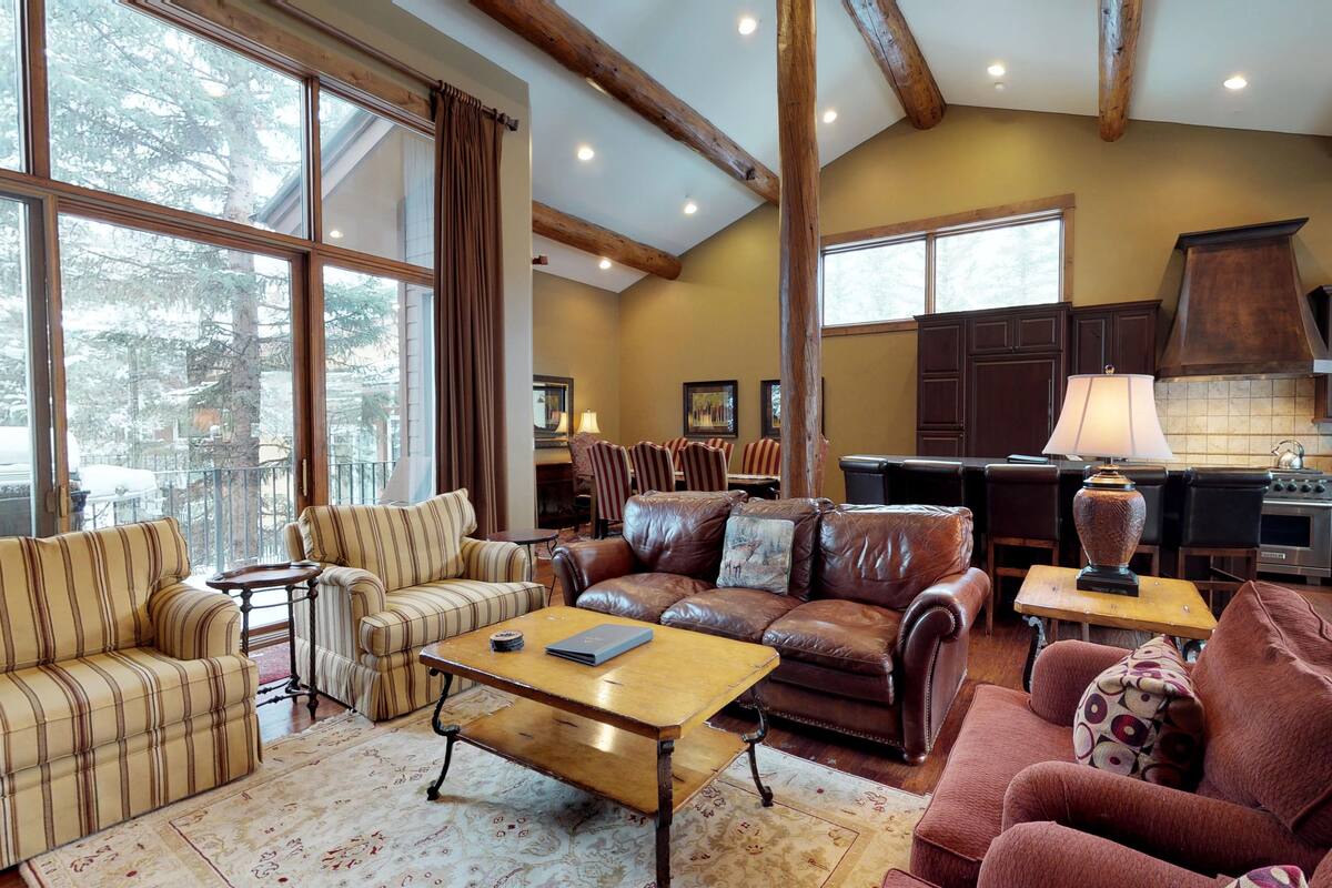 A spacious living room with large windows, a fireplace, and a kitchen area.