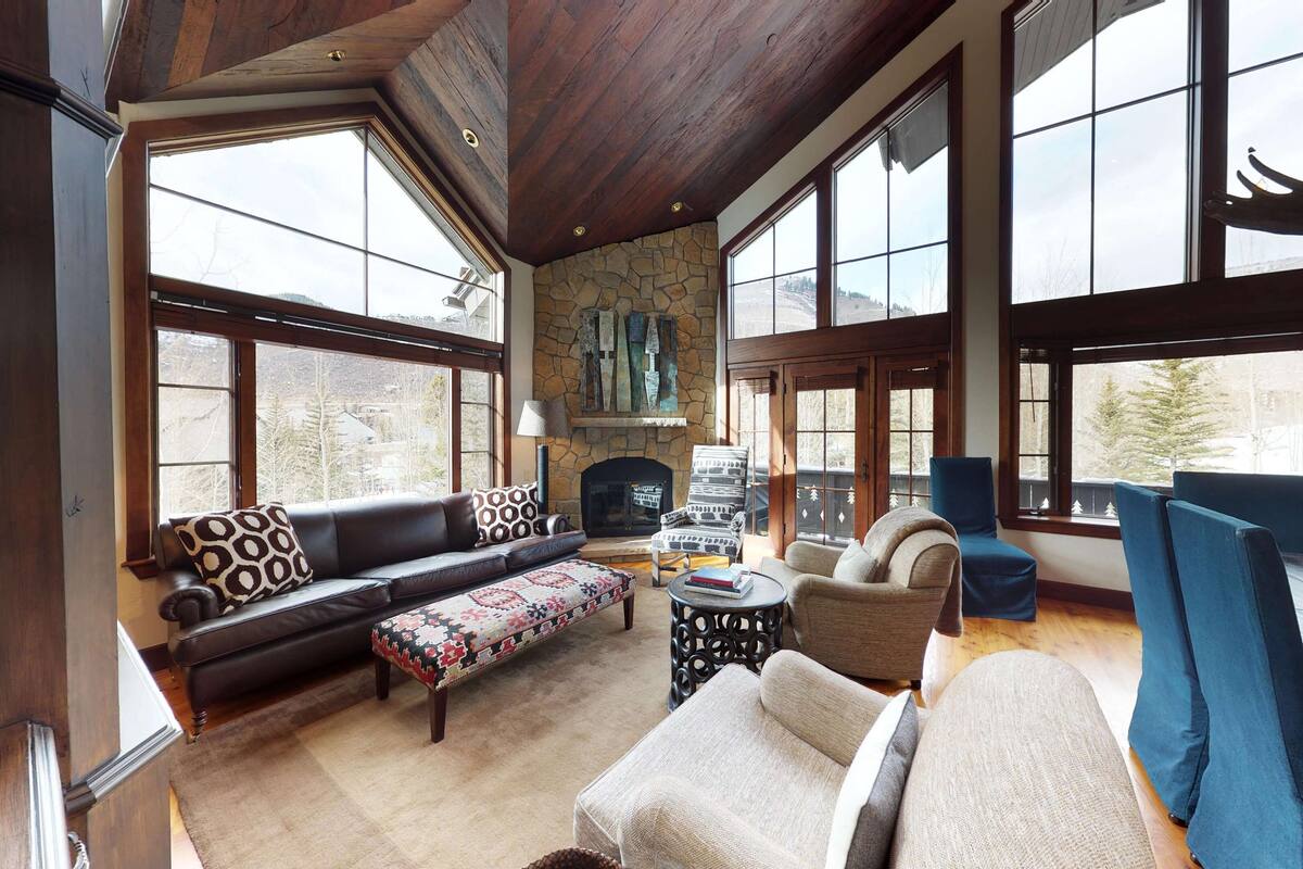 A spacious living room with a stone fireplace, large windows, and a high ceiling.