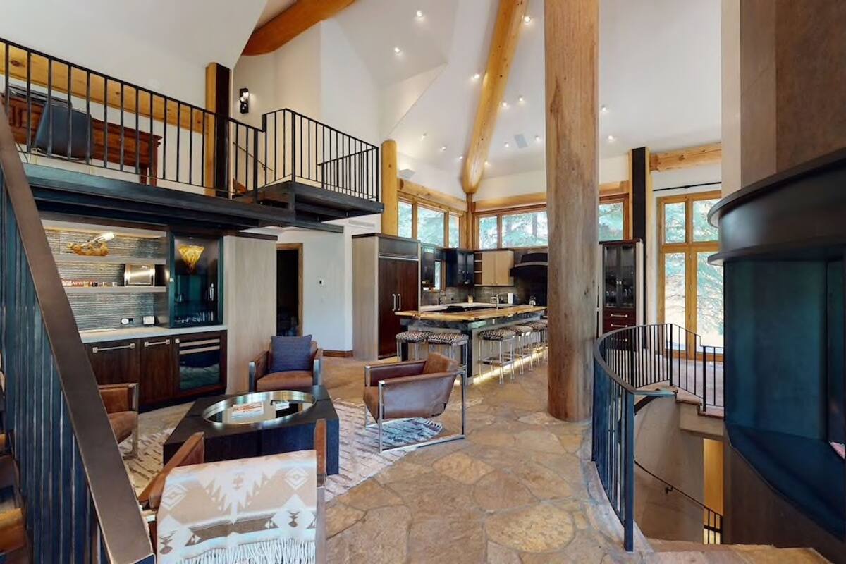 A spacious living area with a high ceiling, a kitchen with a central island, and a staircase leading to an upper level.