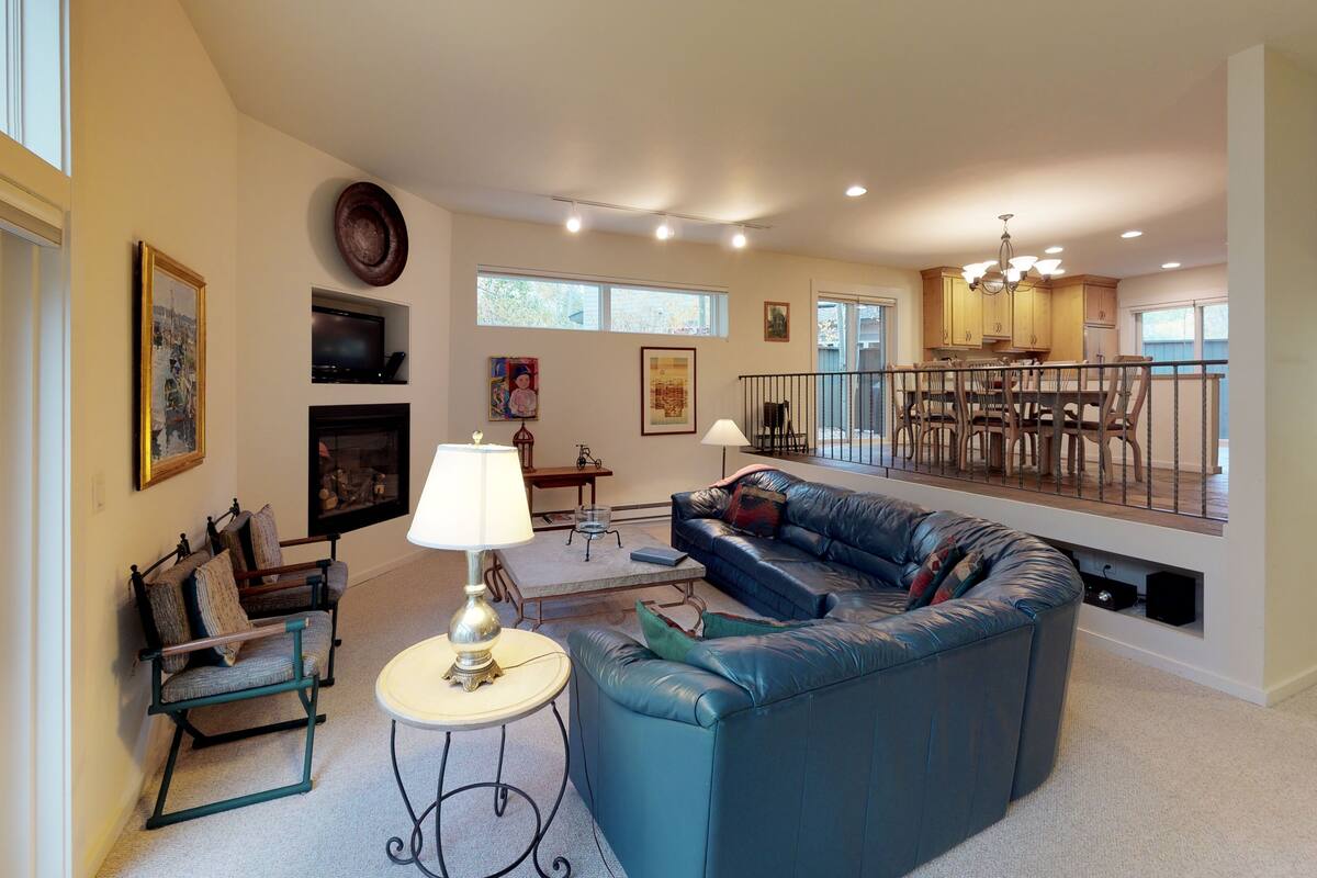 A spacious living room with a blue leather sofa, a fireplace, and a dining area with wooden furniture.
