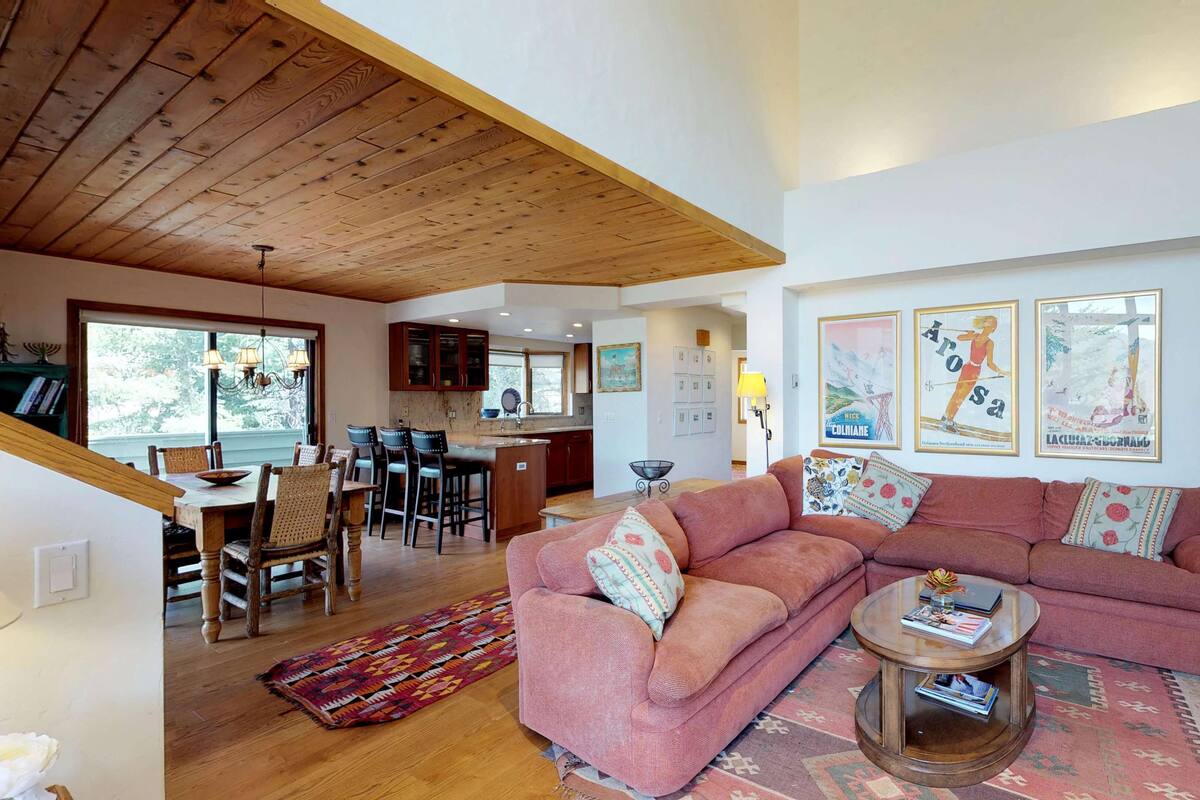 A spacious living room with a large pink sofa, a coffee table, and a dining area with wooden chairs and a table.