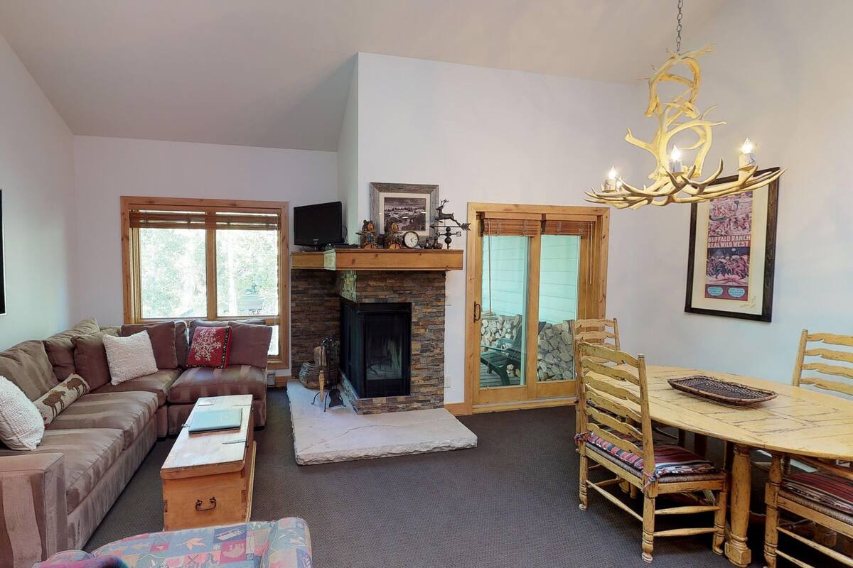 A cozy living room with a sofa, a fireplace, a dining table with chairs, and a television on a stand.