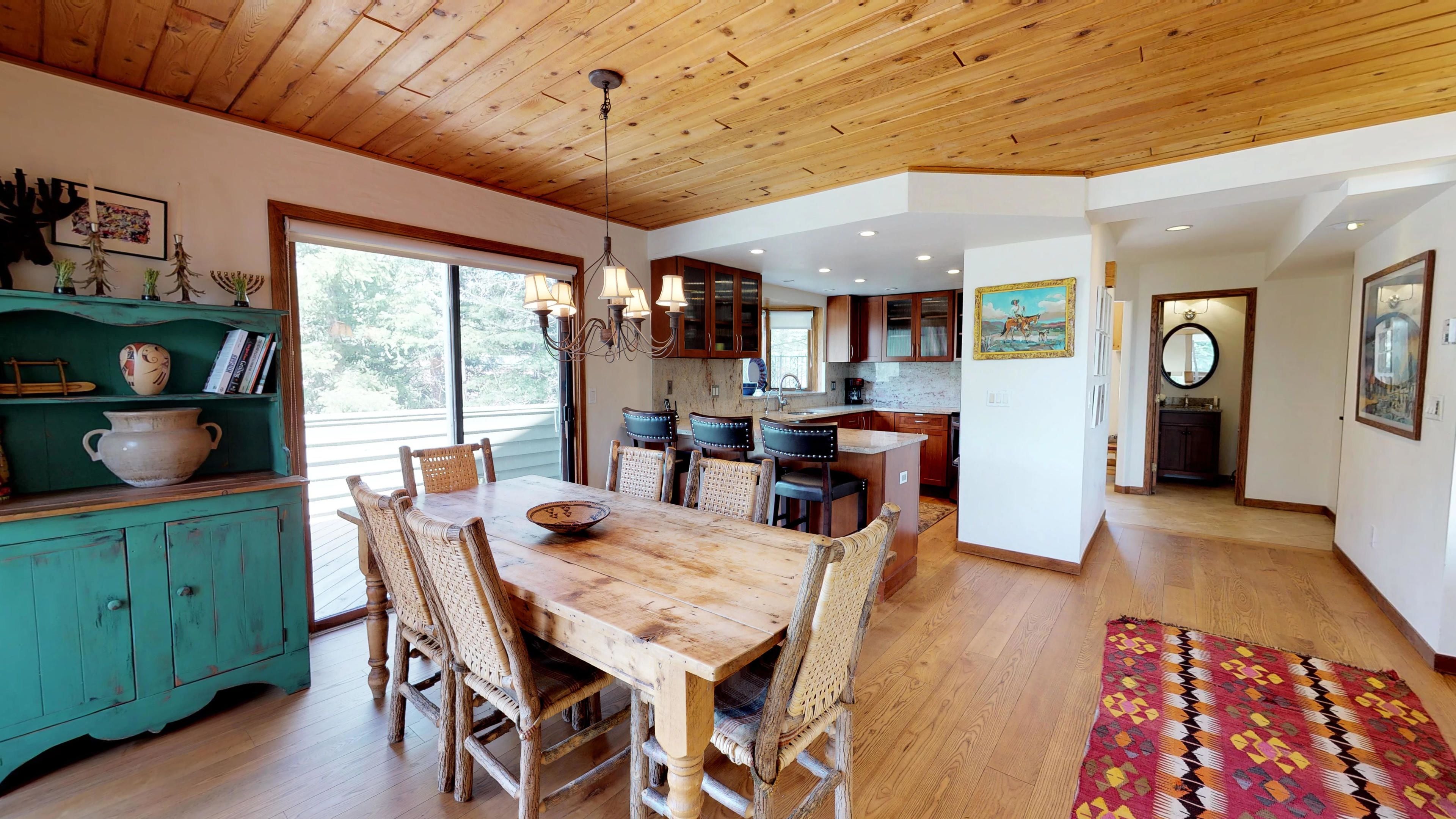 Una cocina amplia con armarios de madera, un comedor con una gran mesa de madera y sillas de mimbre, y vistas al exterior a través de ventanas grandes.