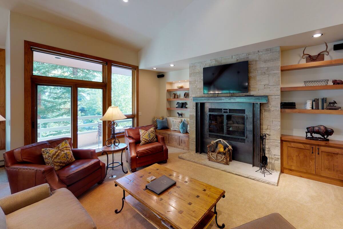 A spacious living room with a fireplace, leather sofas, a coffee table, and wooden shelves with decorative items.
