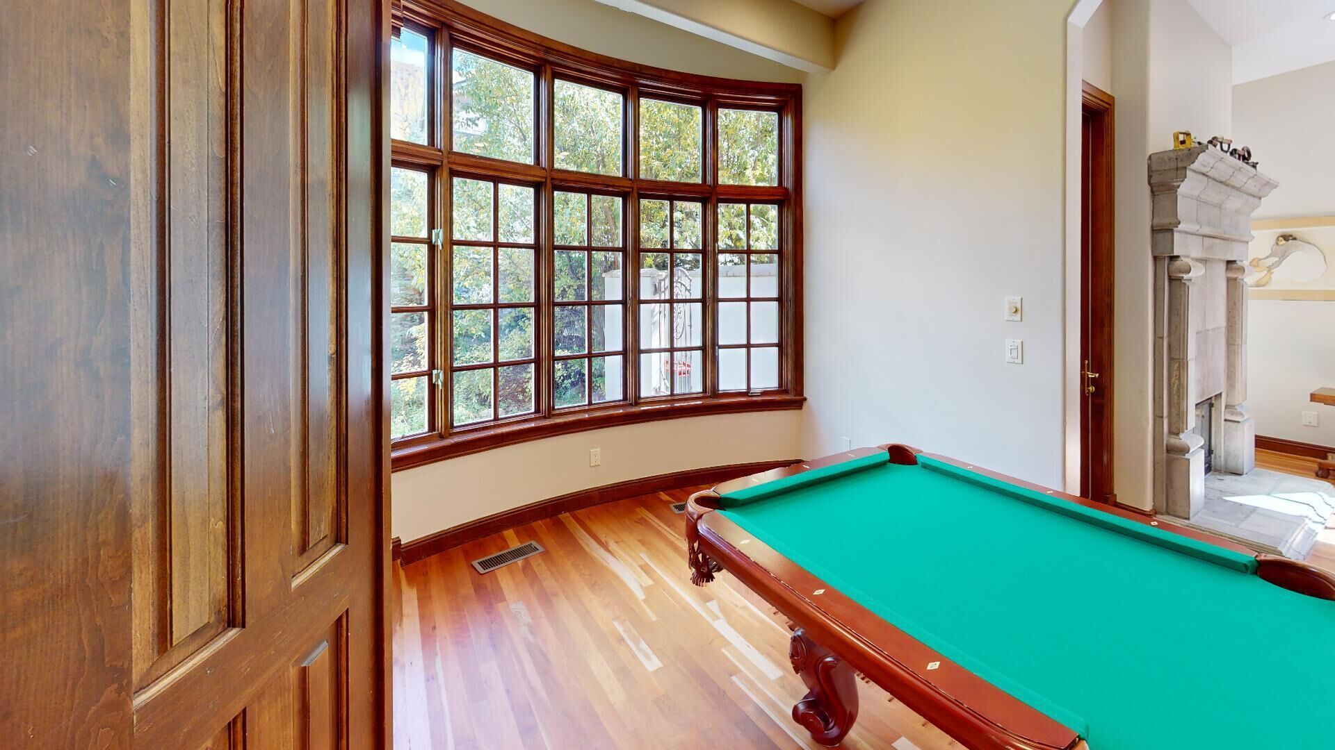 A pool table in a room with wooden flooring and large windows.