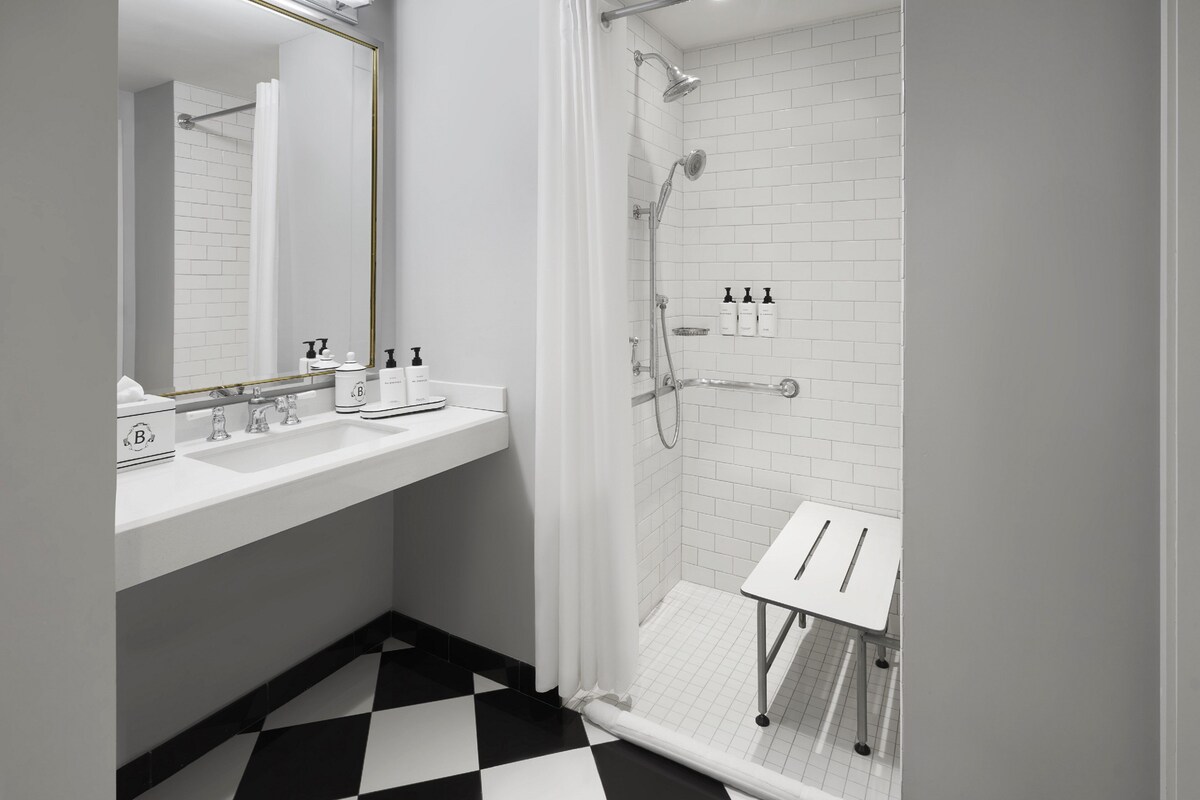 A modern bathroom with a black and white checkered floor, a white sink with two faucets, a mirror, and a shower area with a glass door.