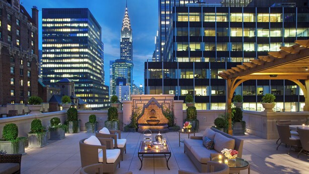 A rooftop terrace with outdoor seating, a decorative fireplace, and a view of city buildings. - InterContinental New York Barclay by IHG (New York)