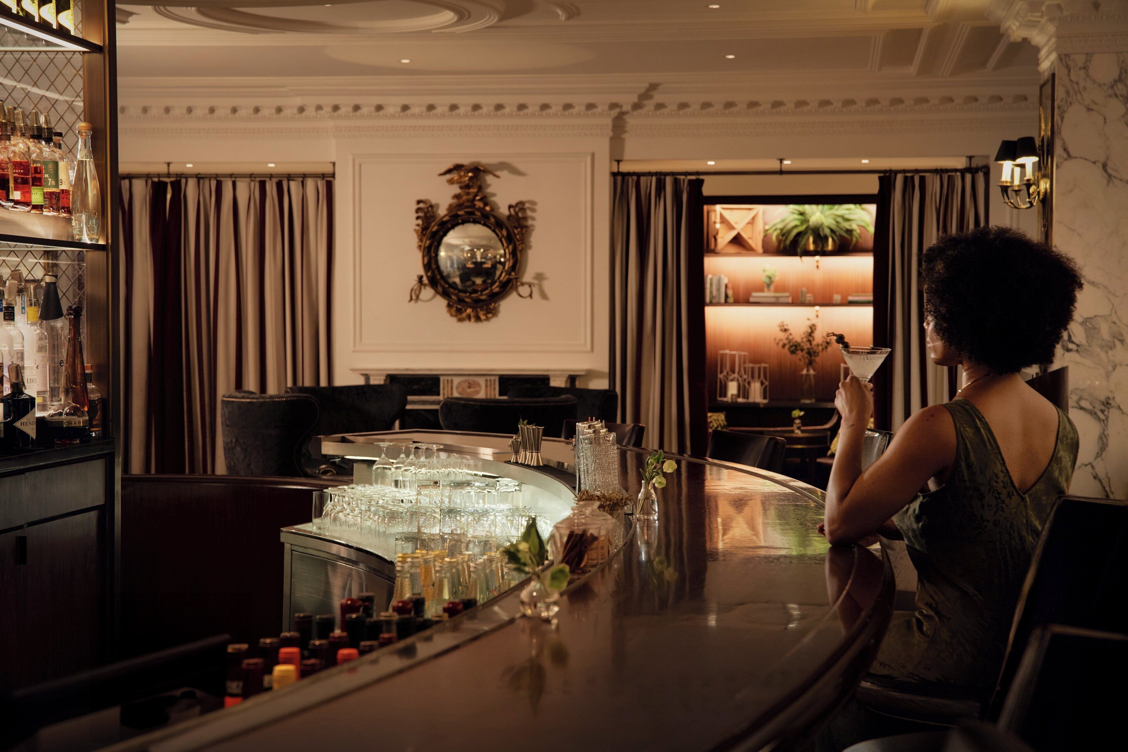 A bar area with a bar counter, glasses, bottles, and a decorative mirror on the wall.