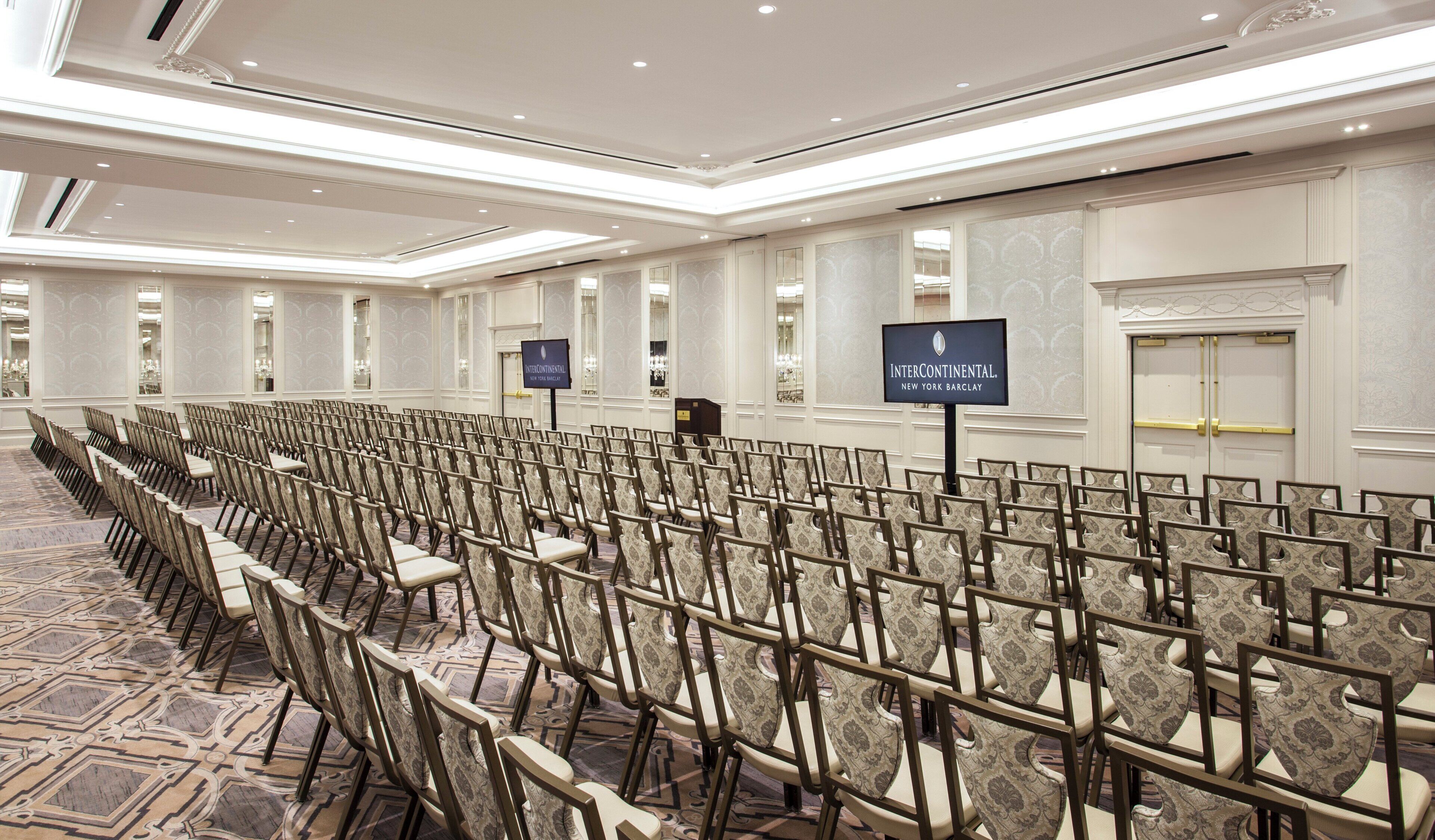 A conference room with rows of chairs, a large screen, and a sign indicating the location.