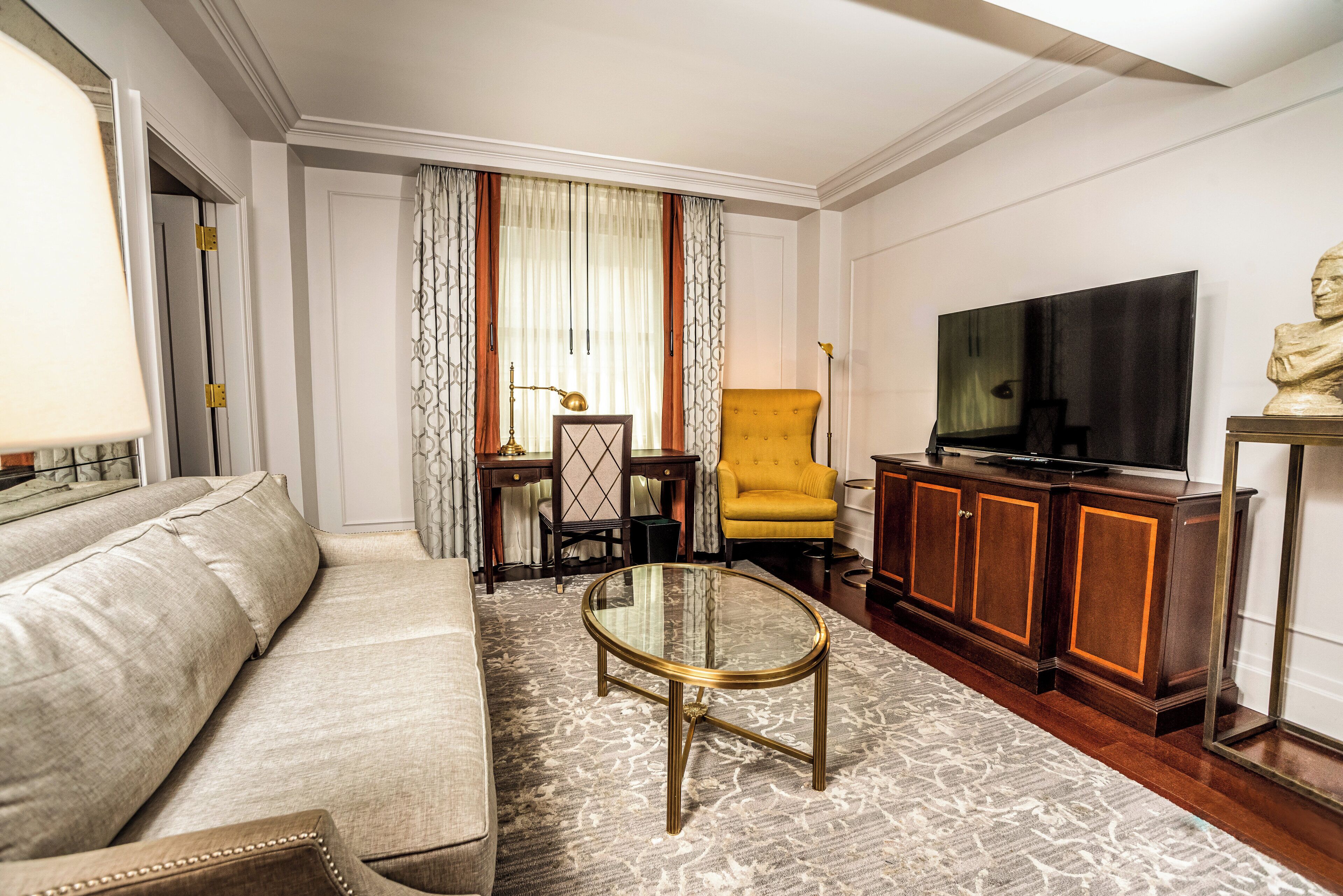 Una sala de estar con un sofá, una mesa de centro de vidrio, un sillón amarillo, un televisor y una estatua.