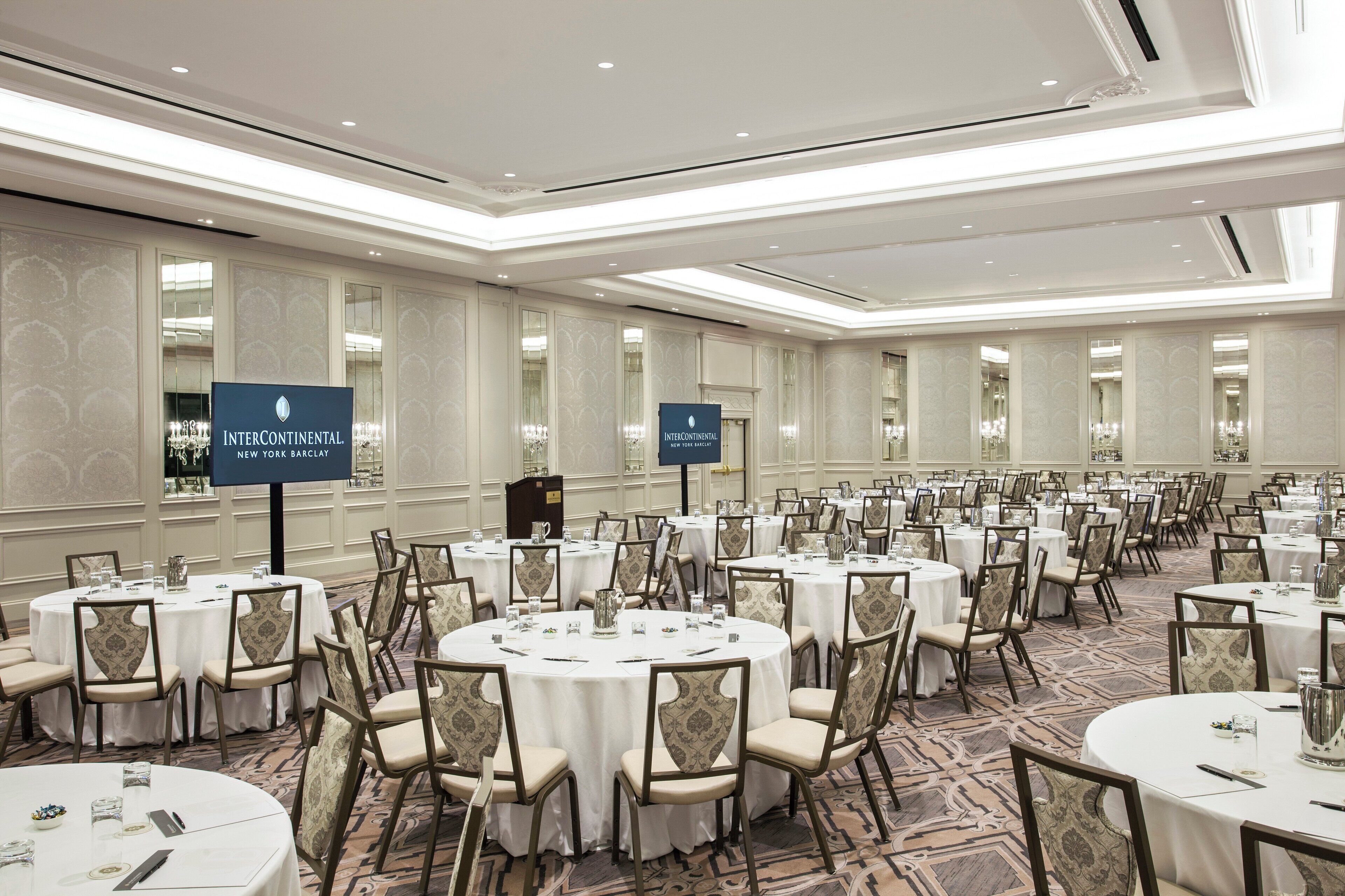 A large conference room with multiple round tables and chairs, arranged in rows.