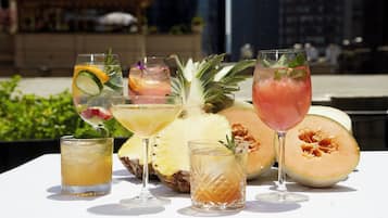 Une table dressée à l’extérieur, sur laquelle on trouve diverses boissons et des fruits, notamment un ananas et un melon.