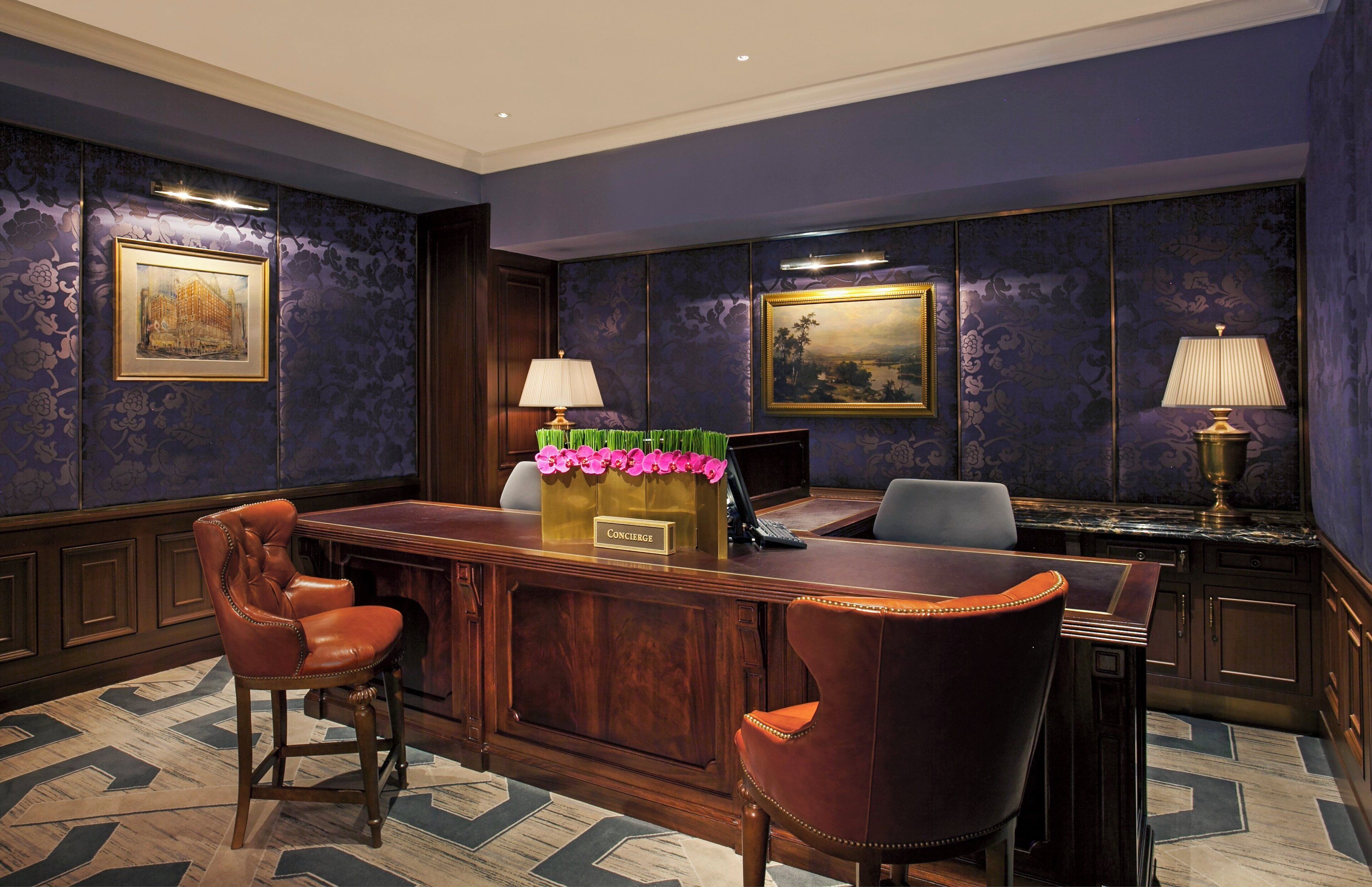 A reception area with a wooden desk, two leather chairs, a framed painting, and a decorative vase with flowers.