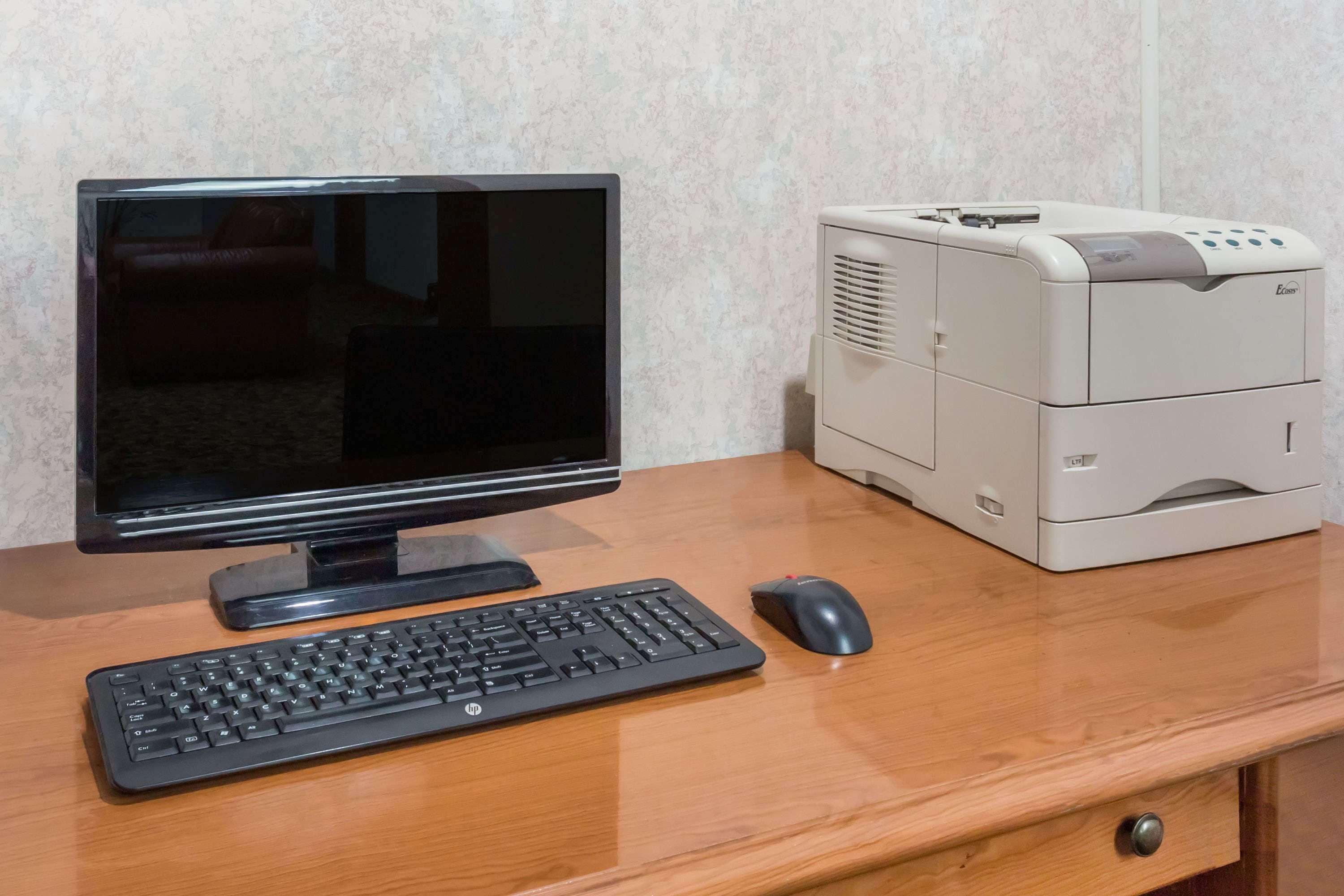 A wooden desk with a desktop computer, including a monitor, keyboard, and mouse, and a printer.