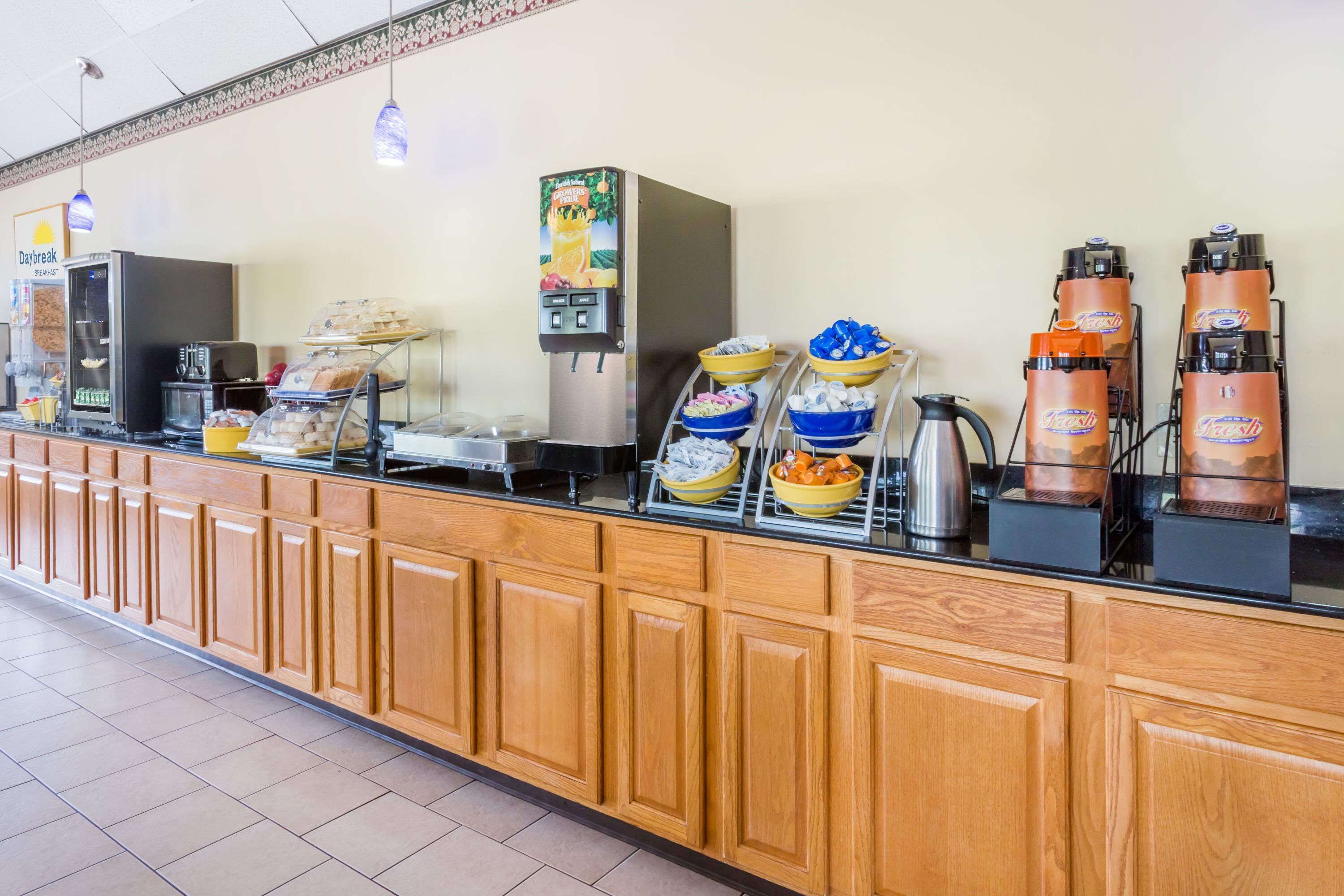A breakfast bar with coffee machines, a fruit dispenser, and various food items.