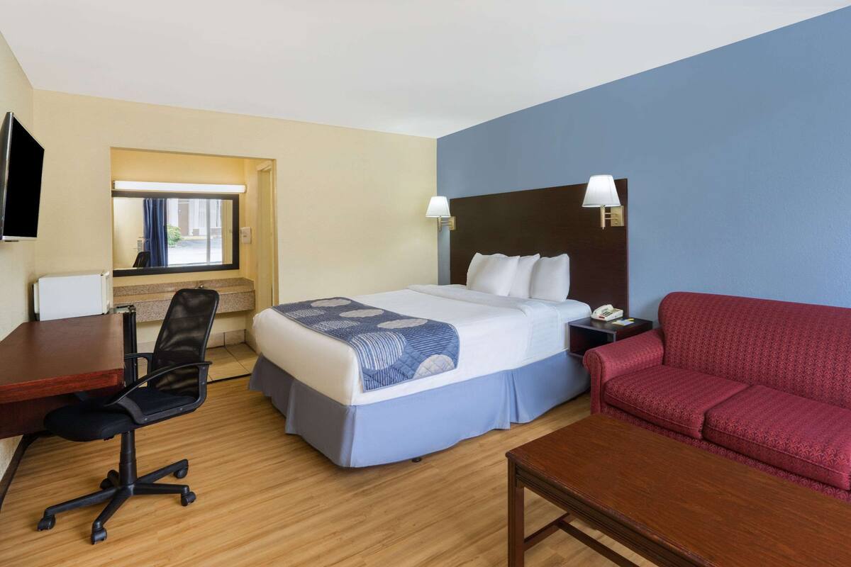 A hotel room with a bed, a desk, a chair, a sofa, and a TV.