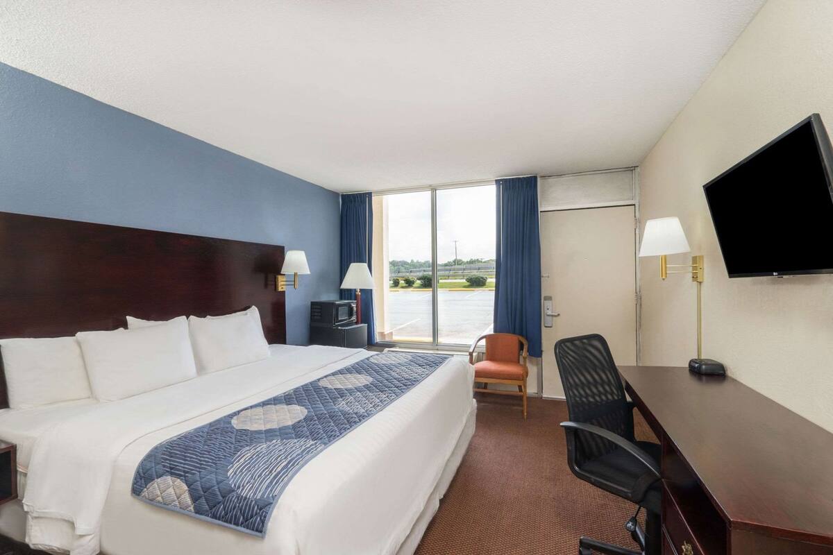 A hotel room with a large bed, a desk, a chair, a TV, and a view of the outdoors.