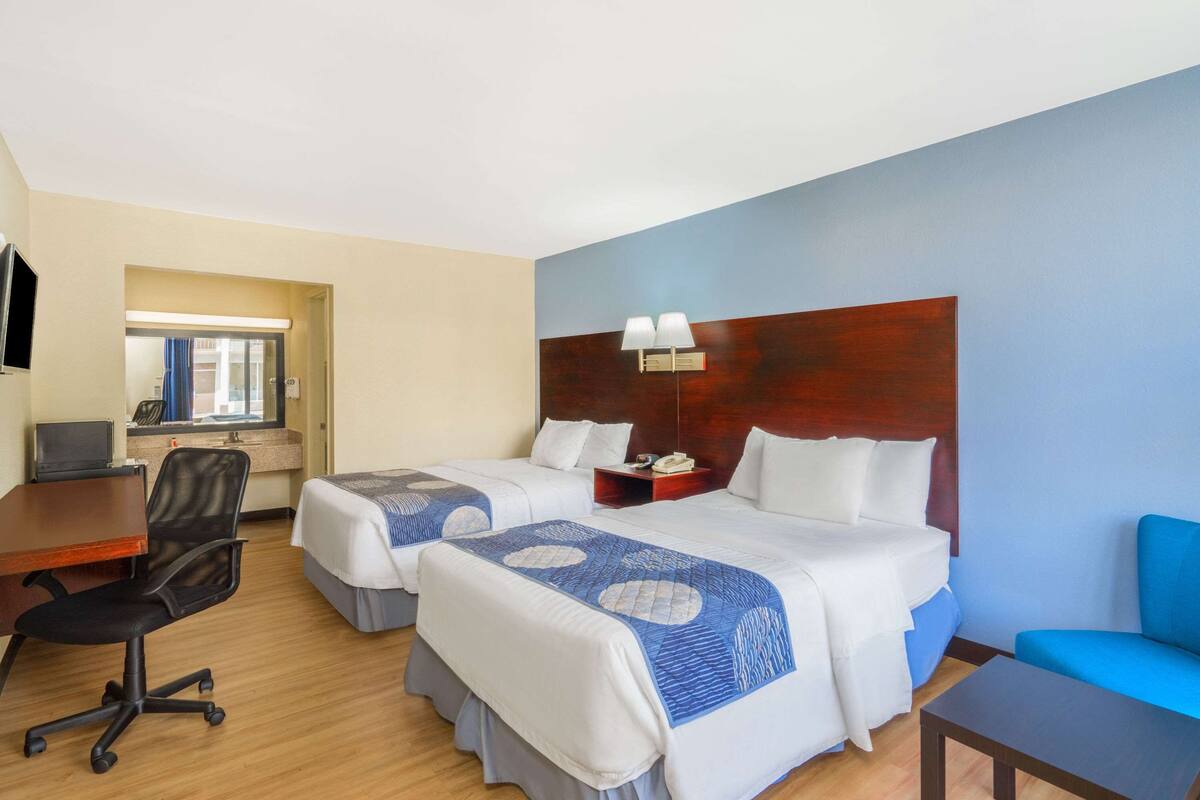 A hotel room with two beds, a desk with a computer, a chair, and a TV.