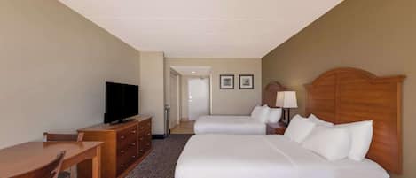 A hotel room with two beds, a desk, a television, and a dresser.
