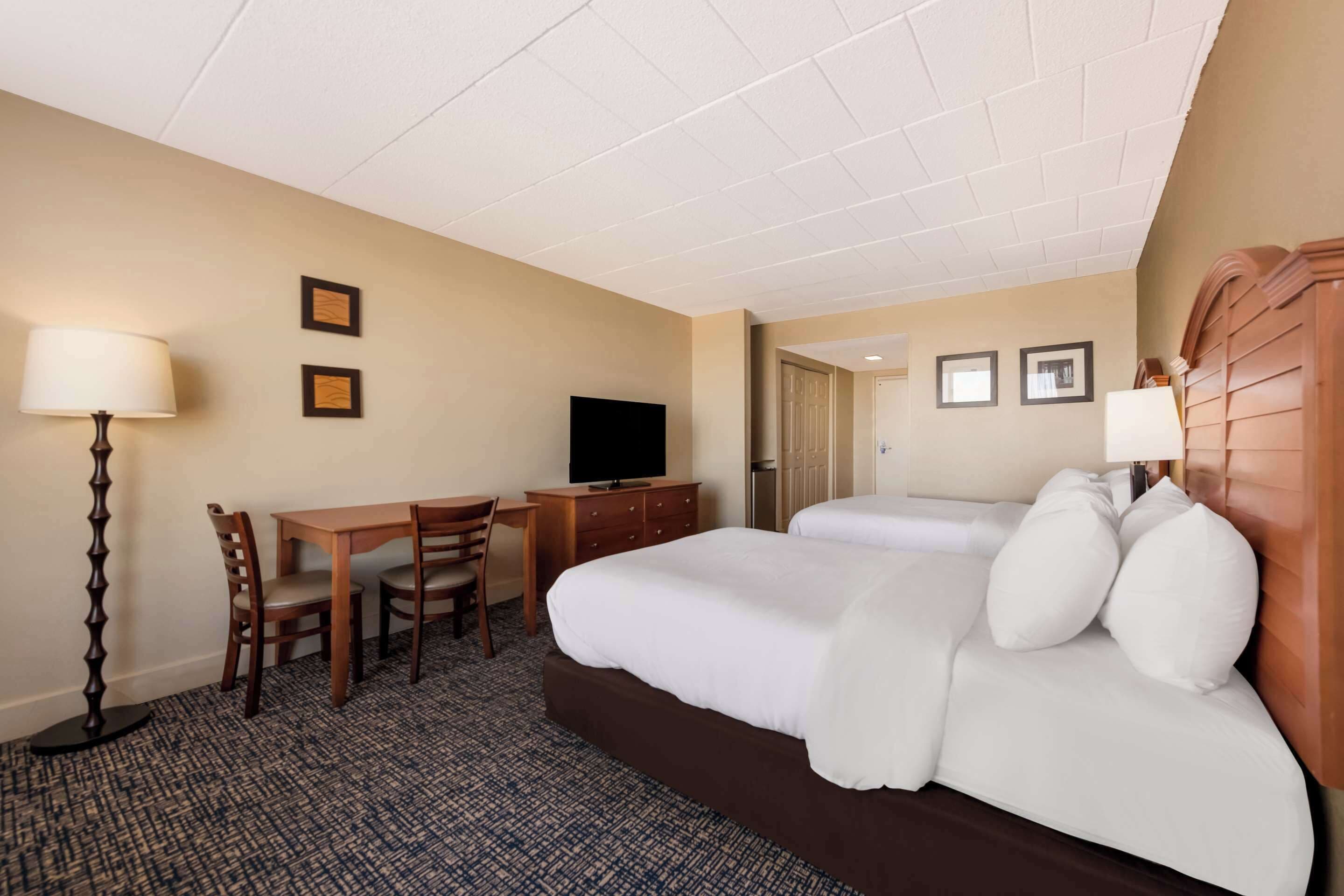 A hotel room with a bed, a desk, a chair, a television, and a lamp.