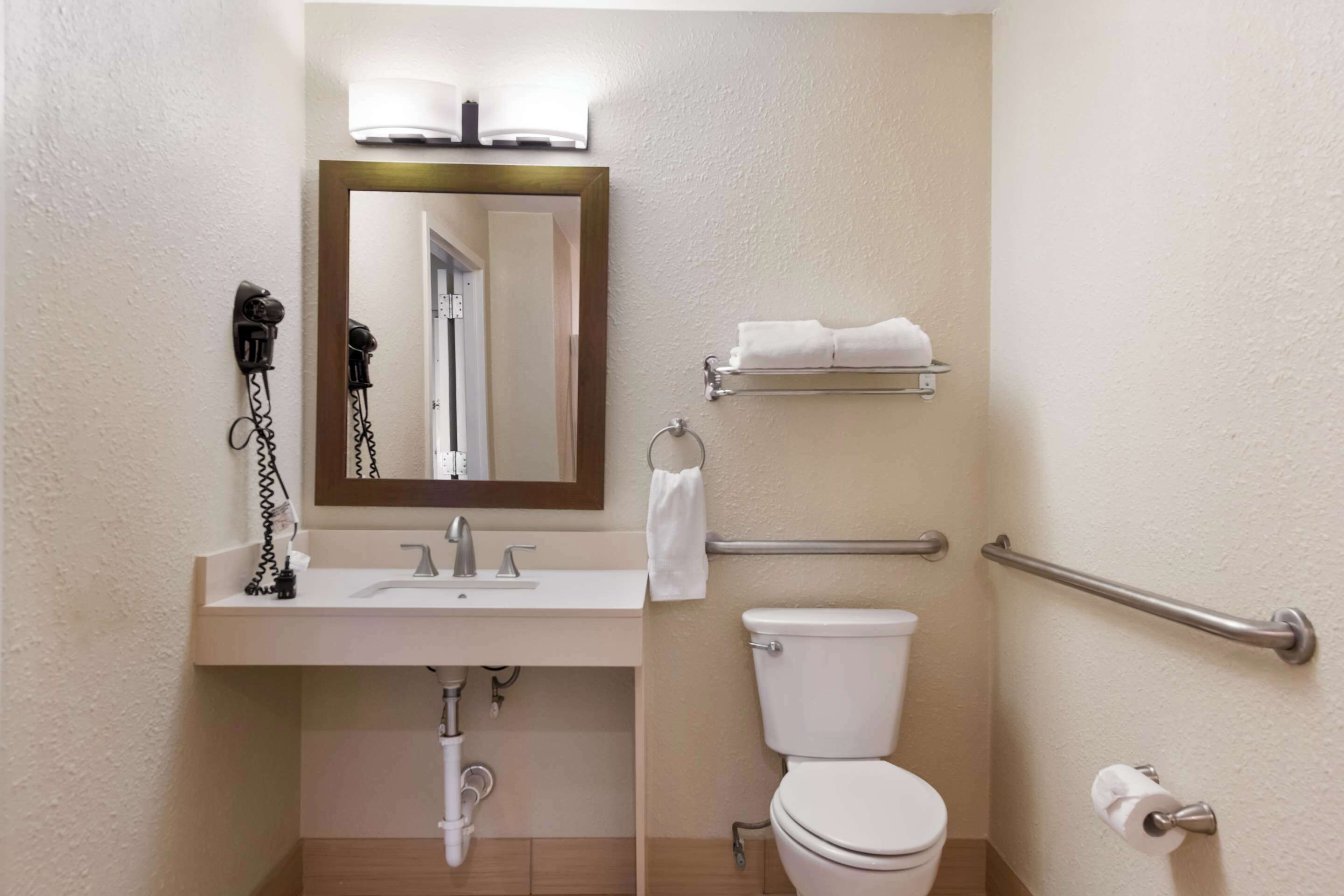 A bathroom with a sink, mirror, toilet, towel rack, and grab bars.