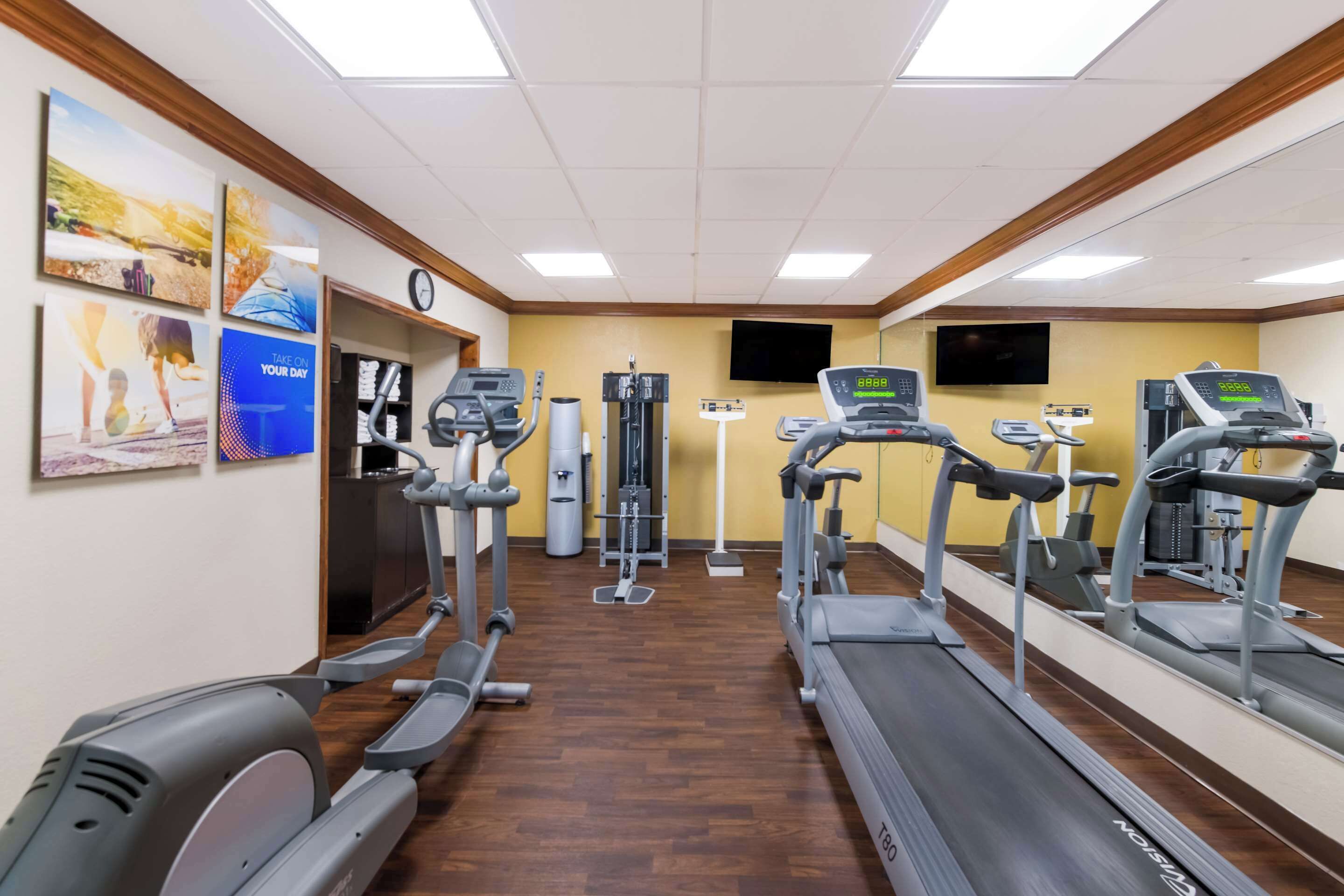 Ein Fitnessraum mit Laufbändern, Crosstrainern und einem Fahrradergometer. An den Wänden hängen motivierende Plakate und eine Uhr befindet sich dort.