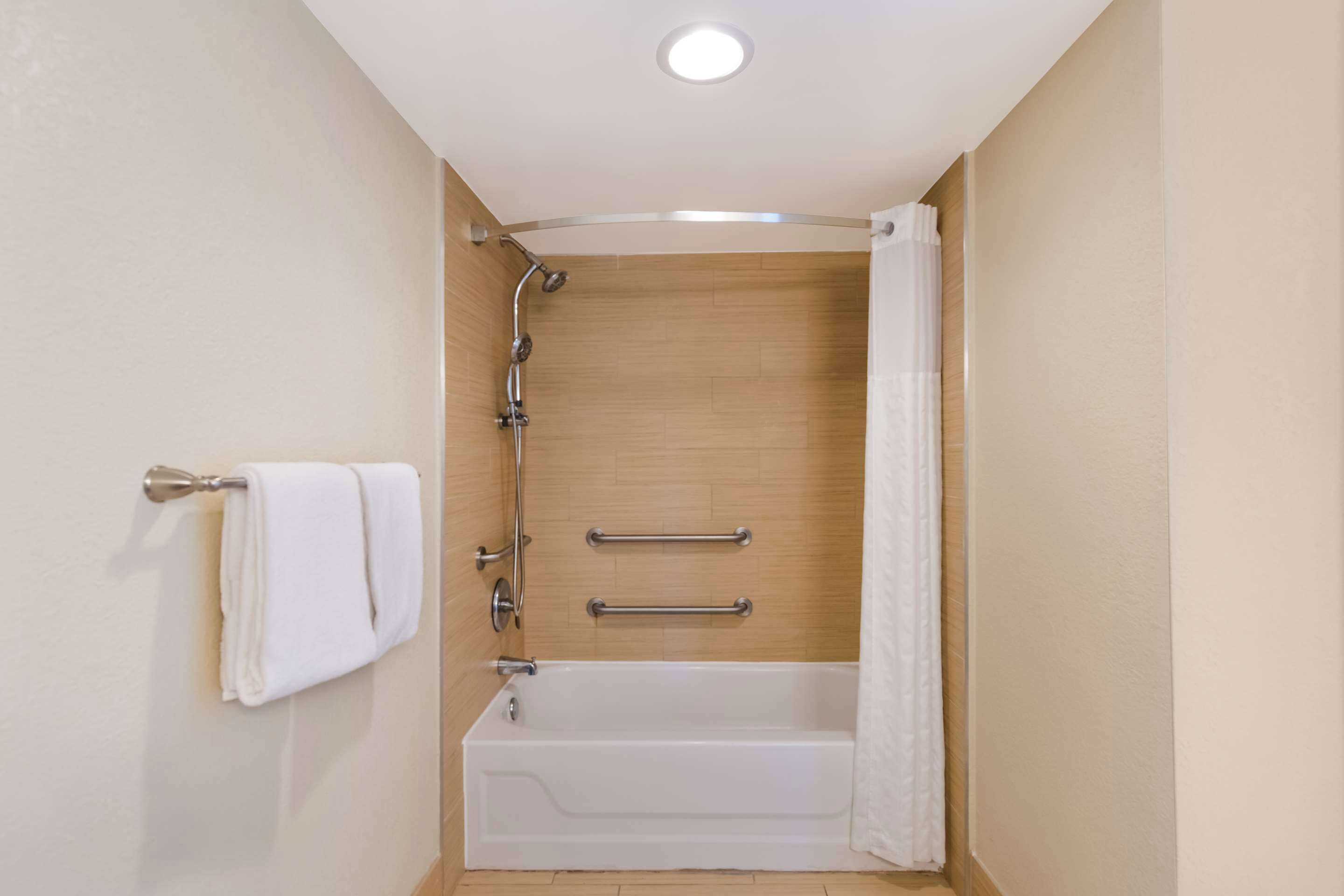 A modern bathroom with a bathtub, shower, and handrails.