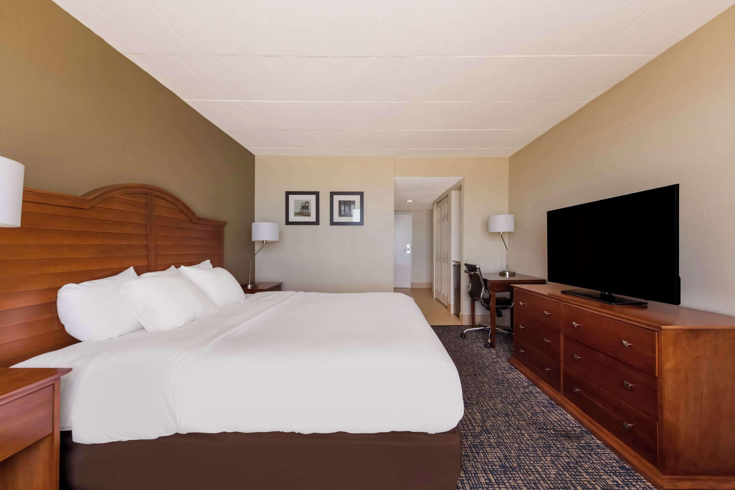 Ein Hotelzimmer mit einem großen Bett, einem Holzkopfteil, einem Flachbildfernseher, einer Kommode und zwei Lampen.