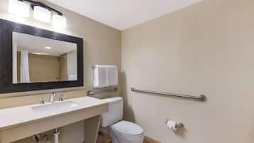 Un baño con lavamanos, espejo, inodoro y barras de apoyo.