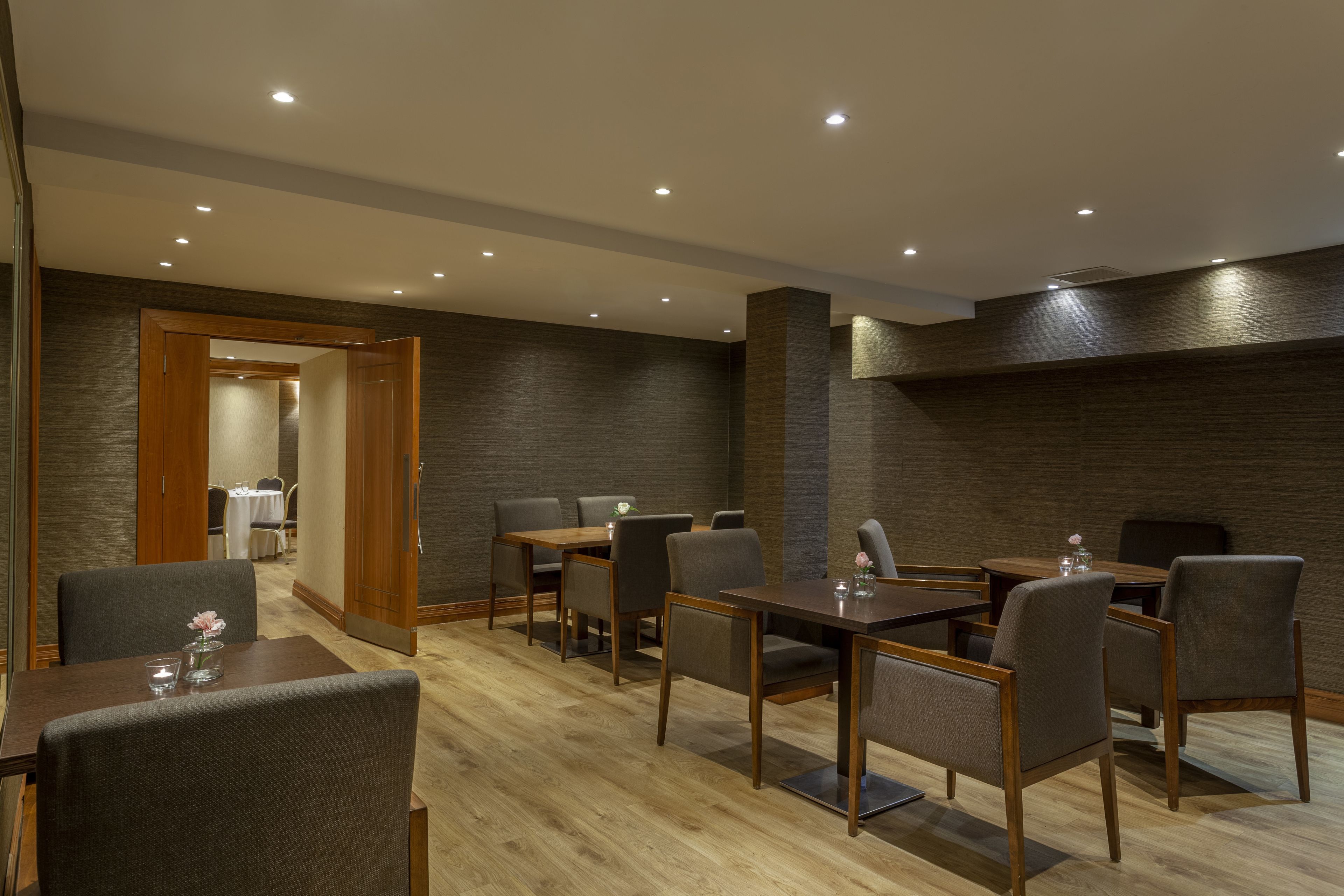 A conference room with multiple tables and chairs, wooden flooring, and recessed ceiling lights.