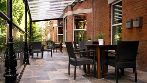 An outdoor patio area with brick walls, wicker furniture, and a glass railing. - The Malone Hotel (Belfast)