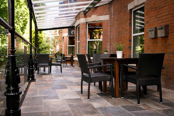 An outdoor patio area with brick walls, wicker furniture, and a glass railing. - The Malone Hotel (Belfast)