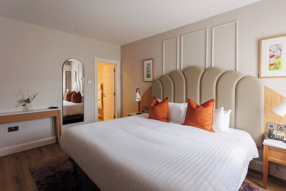 A hotel room with a large bed, a bedside table, a desk, and a mirror.