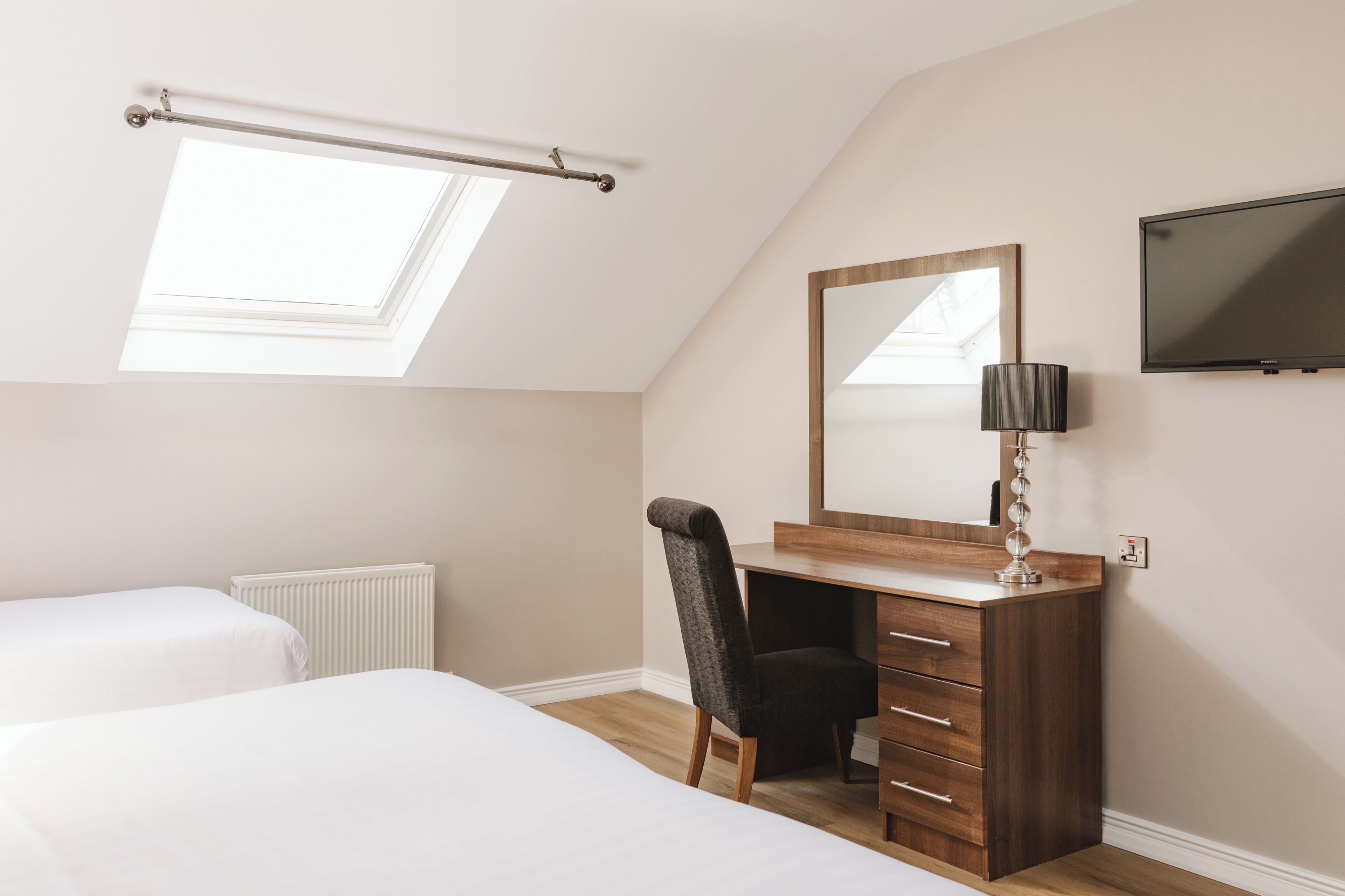 Une chambre avec un puits de lumière, un lit, un bureau avec un miroir, une chaise et un téléviseur.