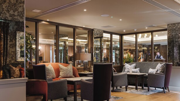 A spacious lobby with a sofa, armchairs, and a coffee table. Large windows offer a view of the interior. - The Malone Hotel (Belfast)