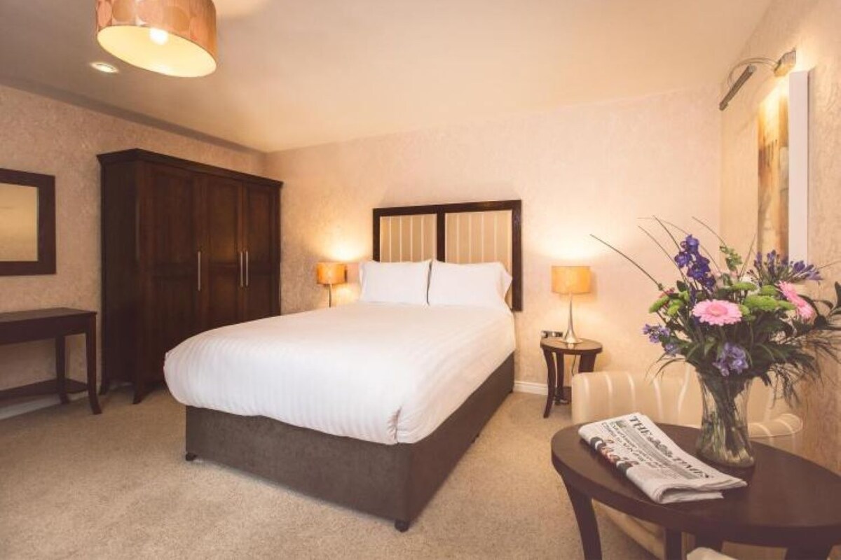 A hotel room with a bed, bedside lamps, a desk with a chair, and a vase of flowers.