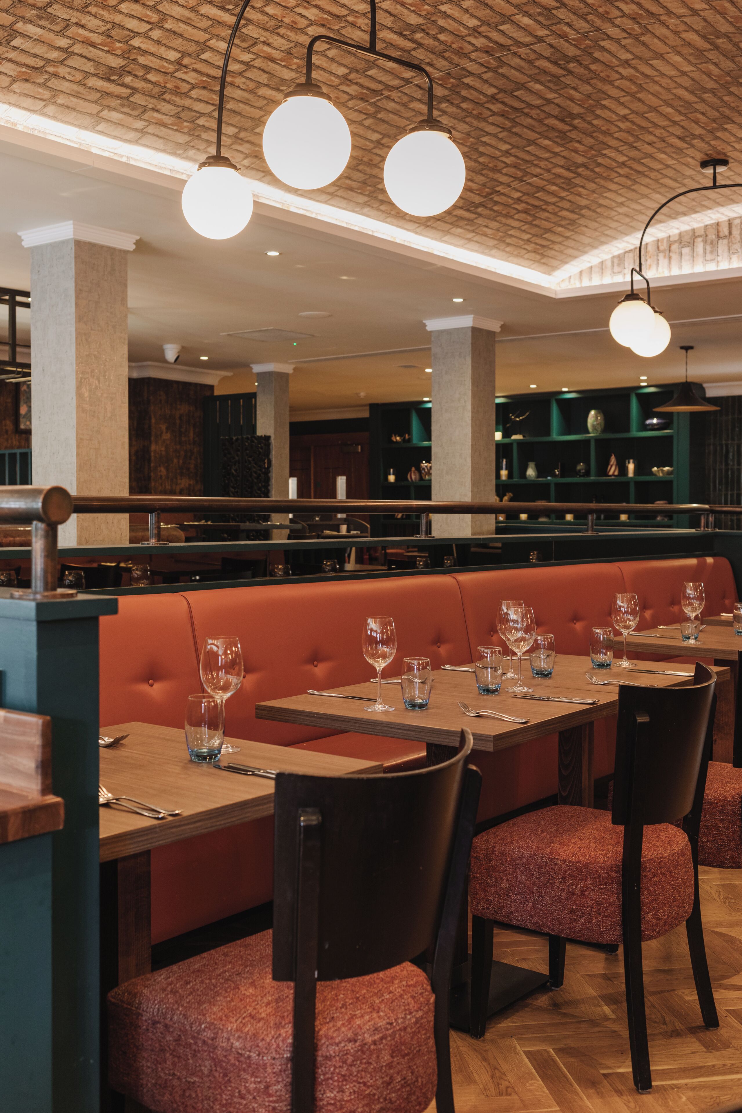 A restaurant interior with wooden tables, red upholstered booths, and hanging pendant lights.