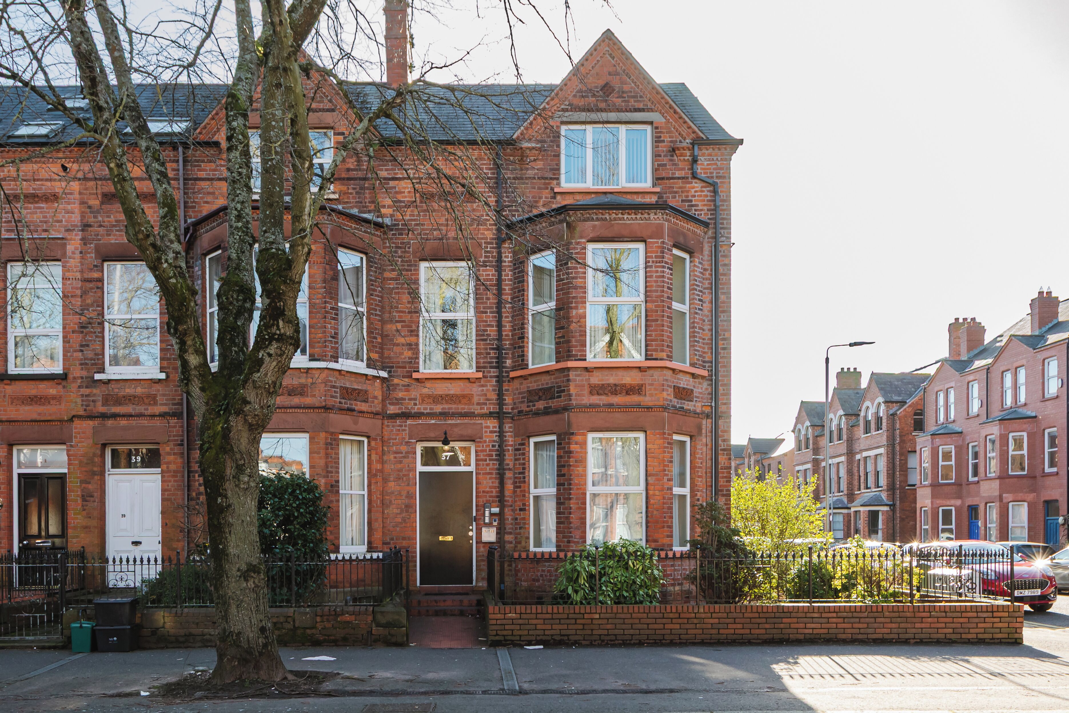 A red brick terraced house with a bay window, a front door, and a small garden area.