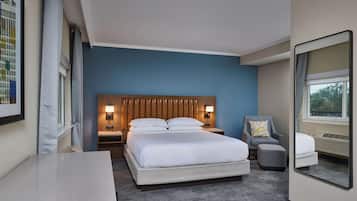 Una habitación de hotel con una cama grande, lámparas de noche, una silla, una mesita y un espejo.