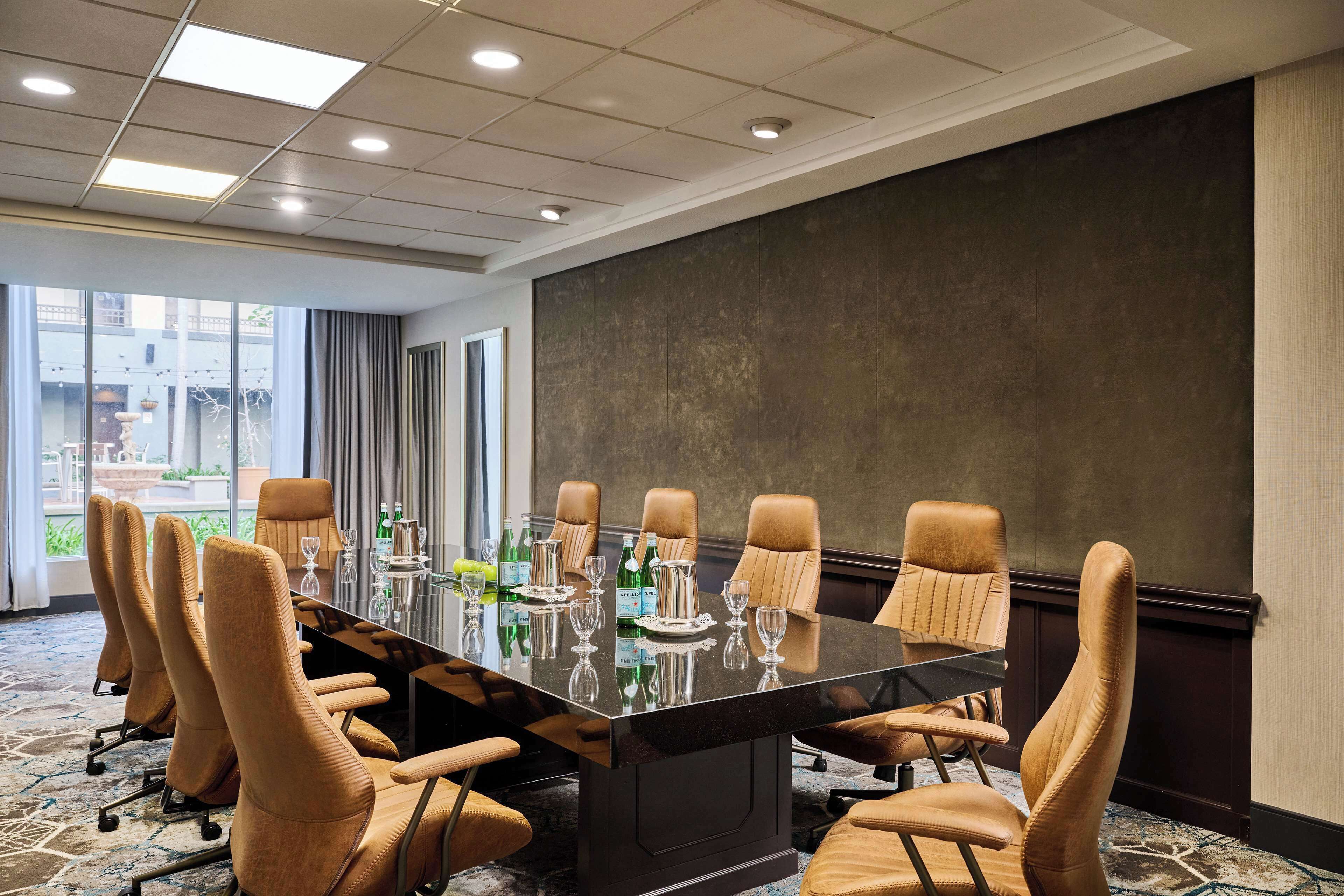 A conference room with a long table, multiple chairs, and a large window offering a view of the outdoors.